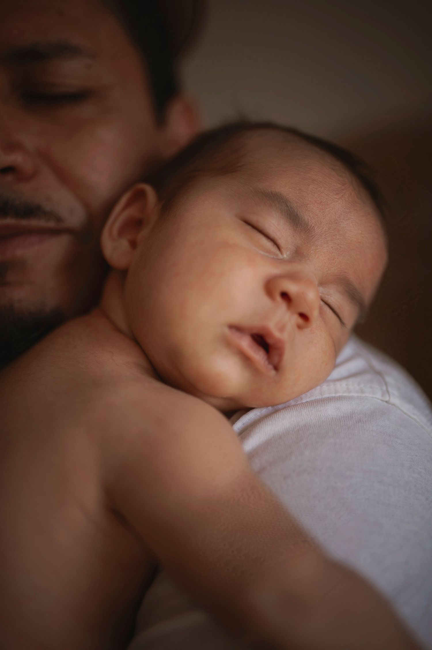 Peaceful sleeping infant resting on caregiver's chest in intimate close-up portrait.