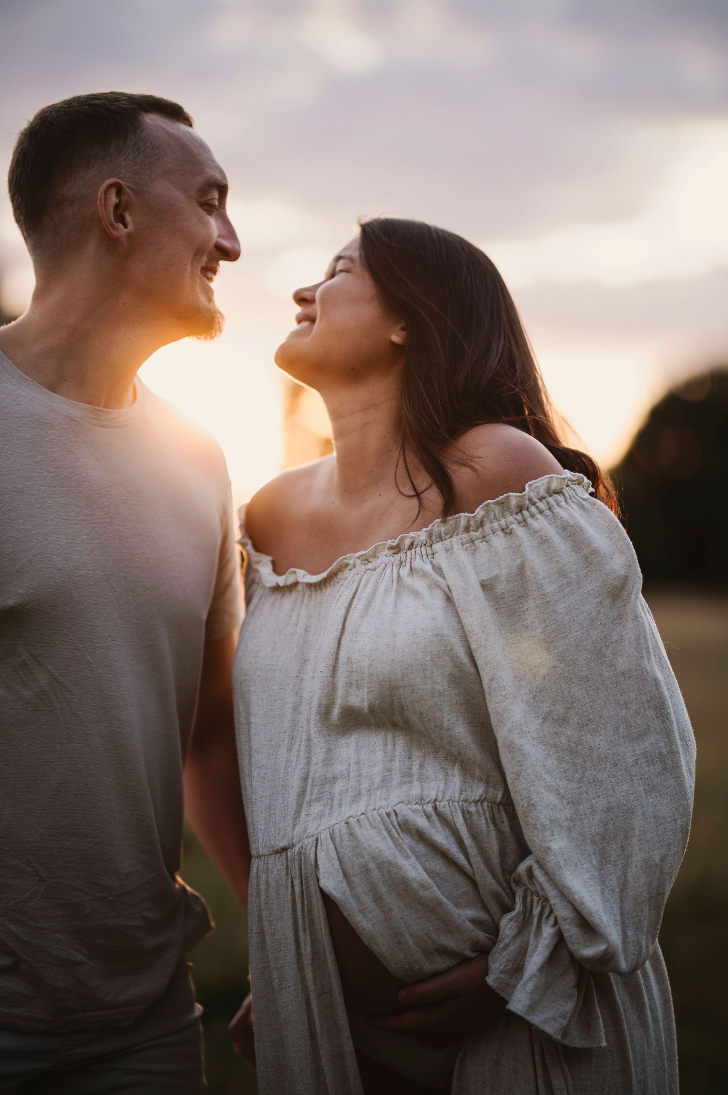 A couple shares an intimate moment at sunset, with the woman wearing a flowing off-shoulder dress.