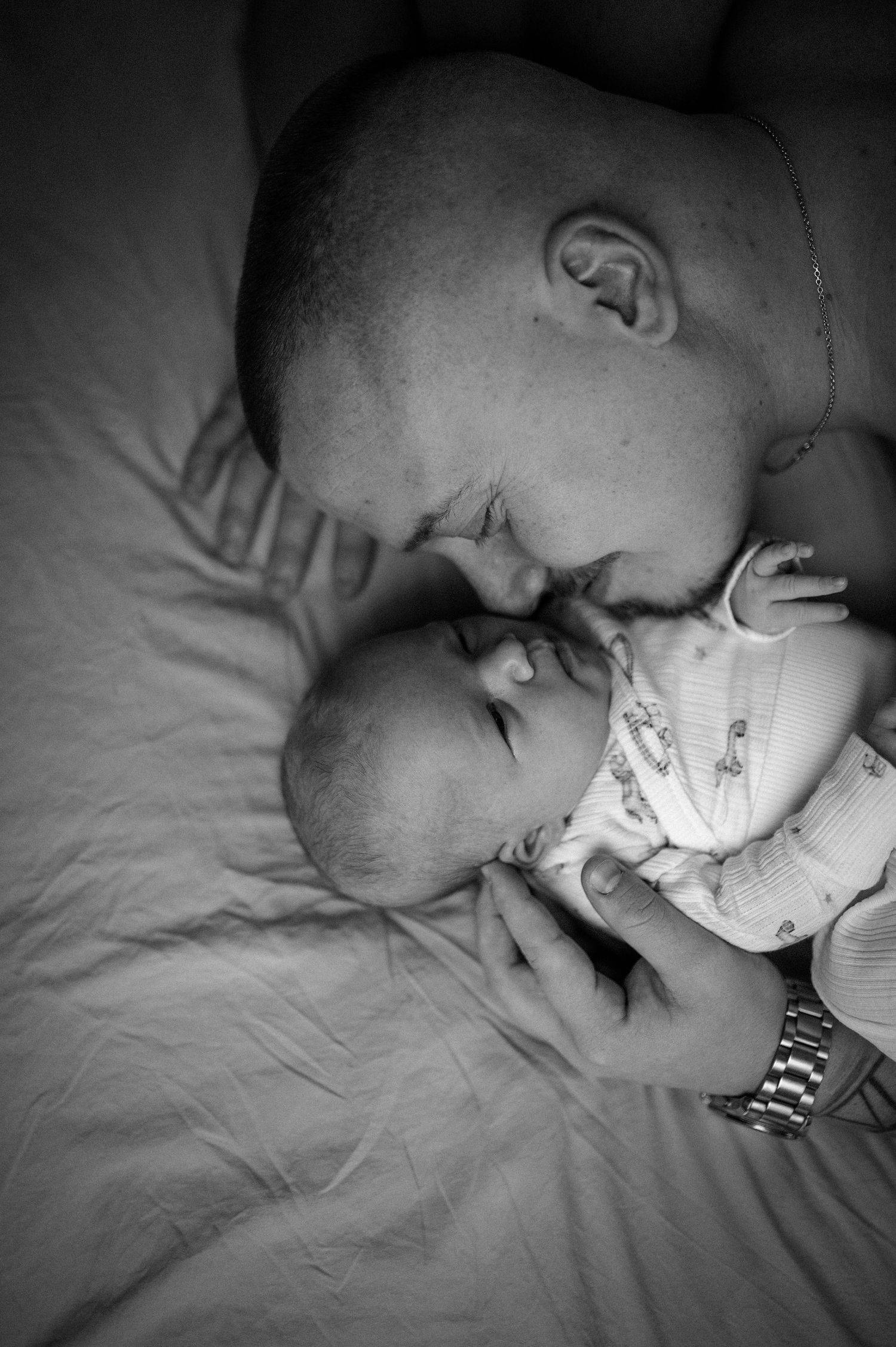 Svartvit nyföddfotografering i Hässleholm med pappa som möter sin nyfödda bebis i en kärleksfull stund i sängen.