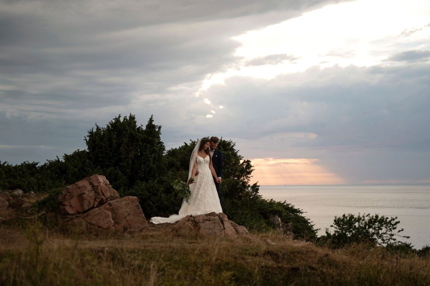 Elopement at Hovs Hallar in Skåne with bride and groom kissing on dramatic coastal cliffs at sunset with moody ocean and cloudy sky.
