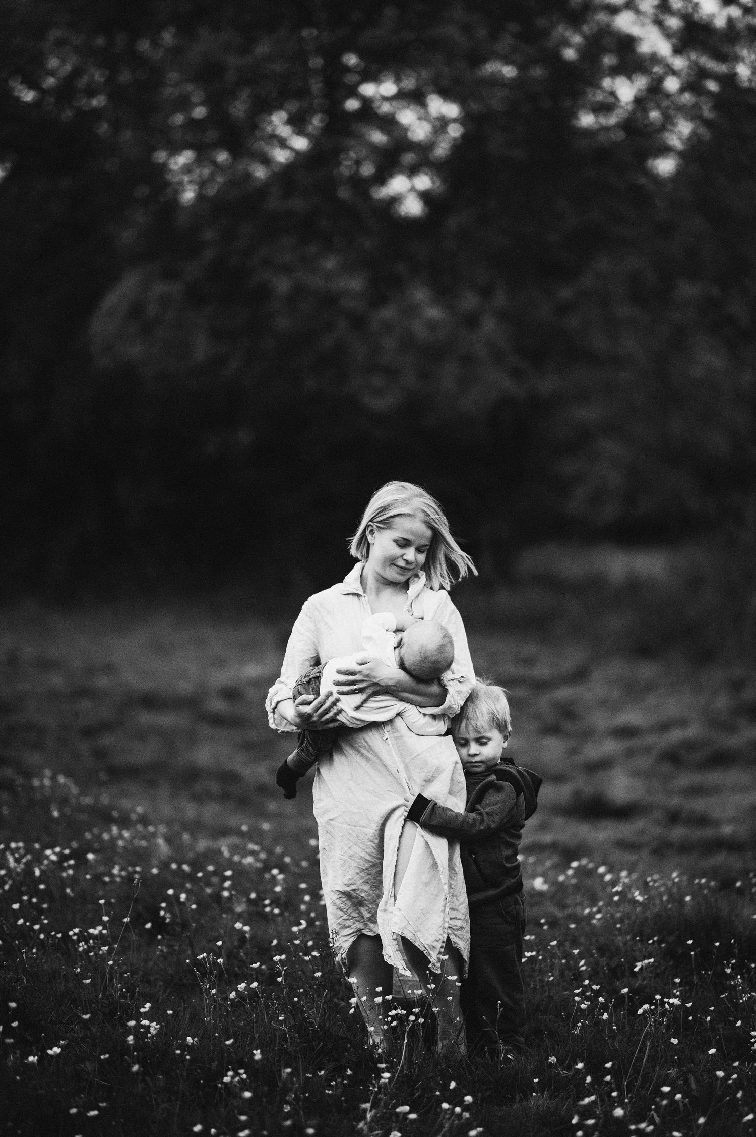 Familjefotografering i Skåne med ammande mamma, nyfödd och småbarn i blomsteräng i svartvitt ljus.