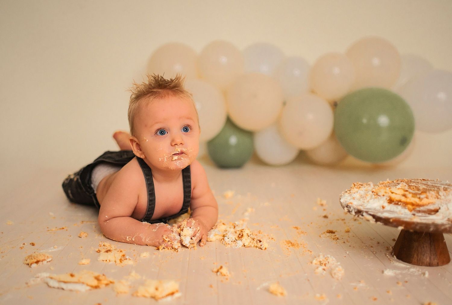 A whimsical cake smash photography session with soft balloon decorations in the background.