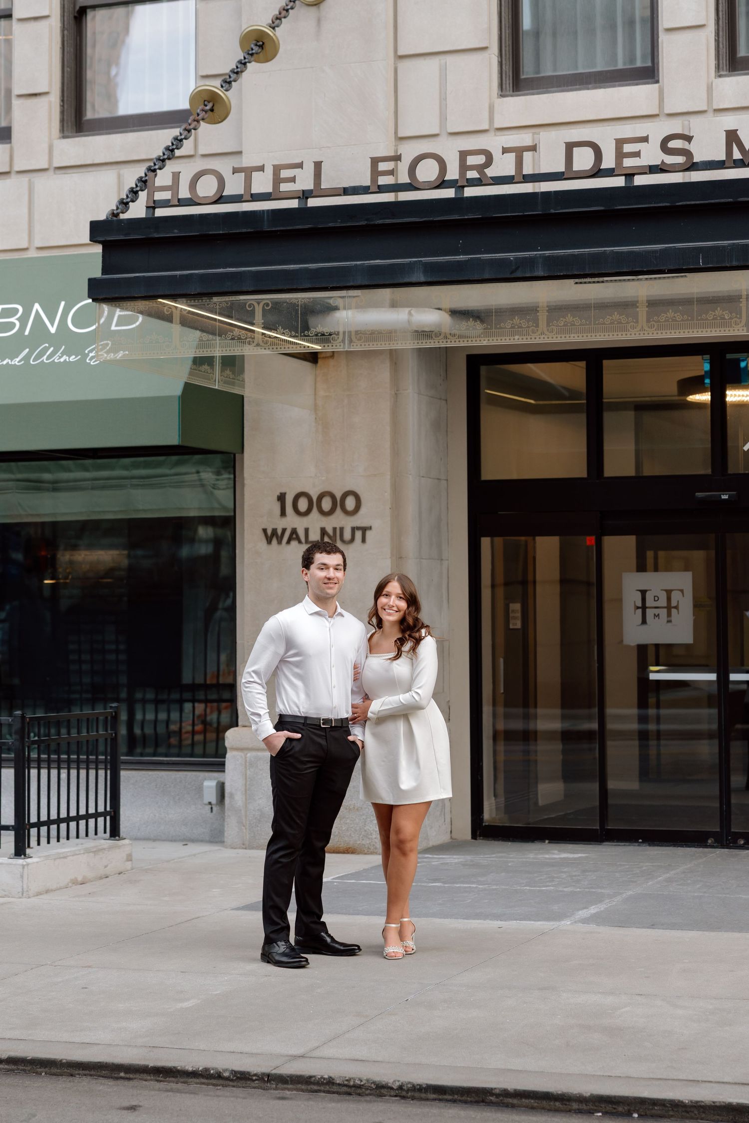 Couple posing in front of Hotel Fort Des Moines at 1000 Walnut Street, man in black pants and woman in white dress.