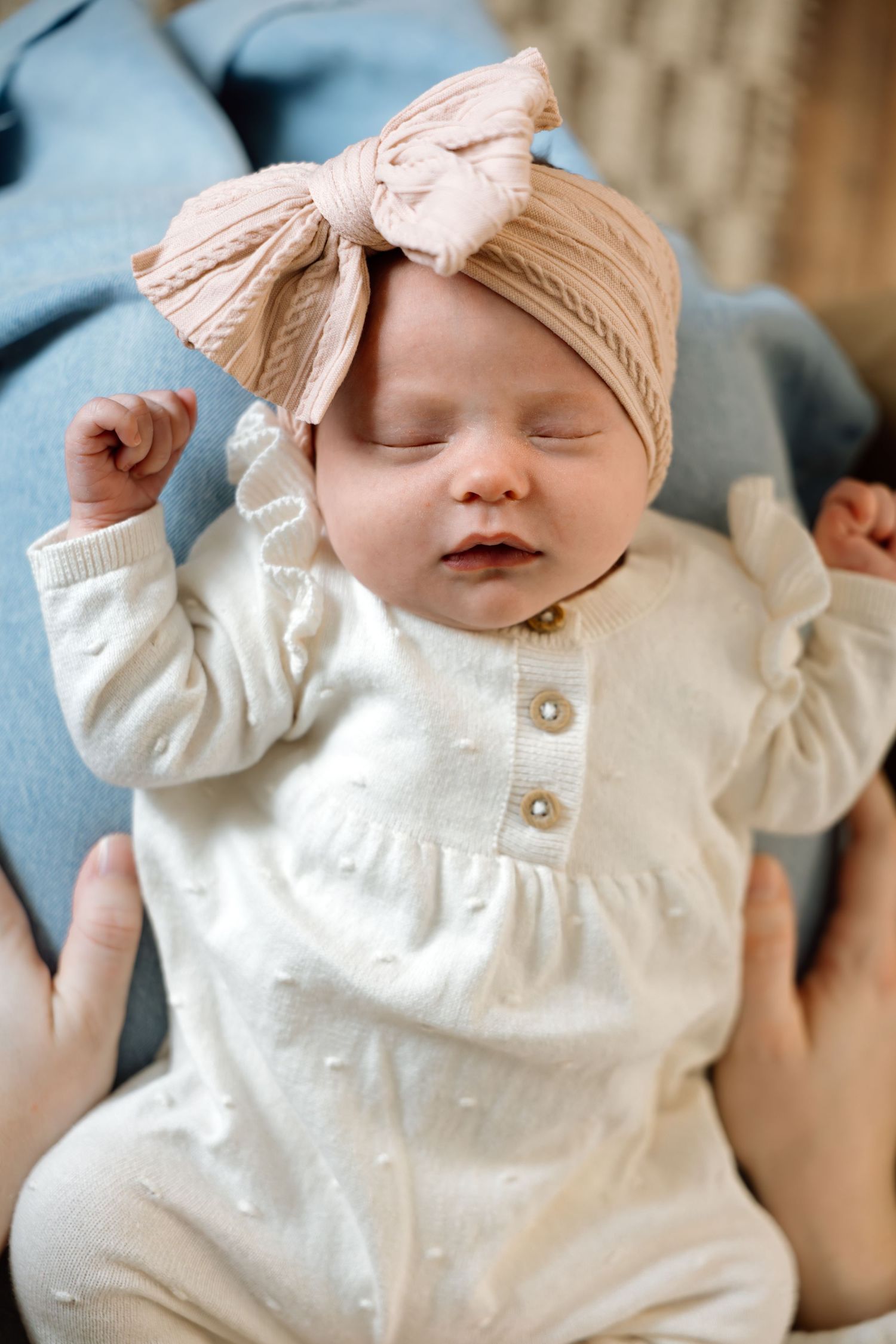 Sleeping newborn girl in white outfit wearing a pink bow turban headband.