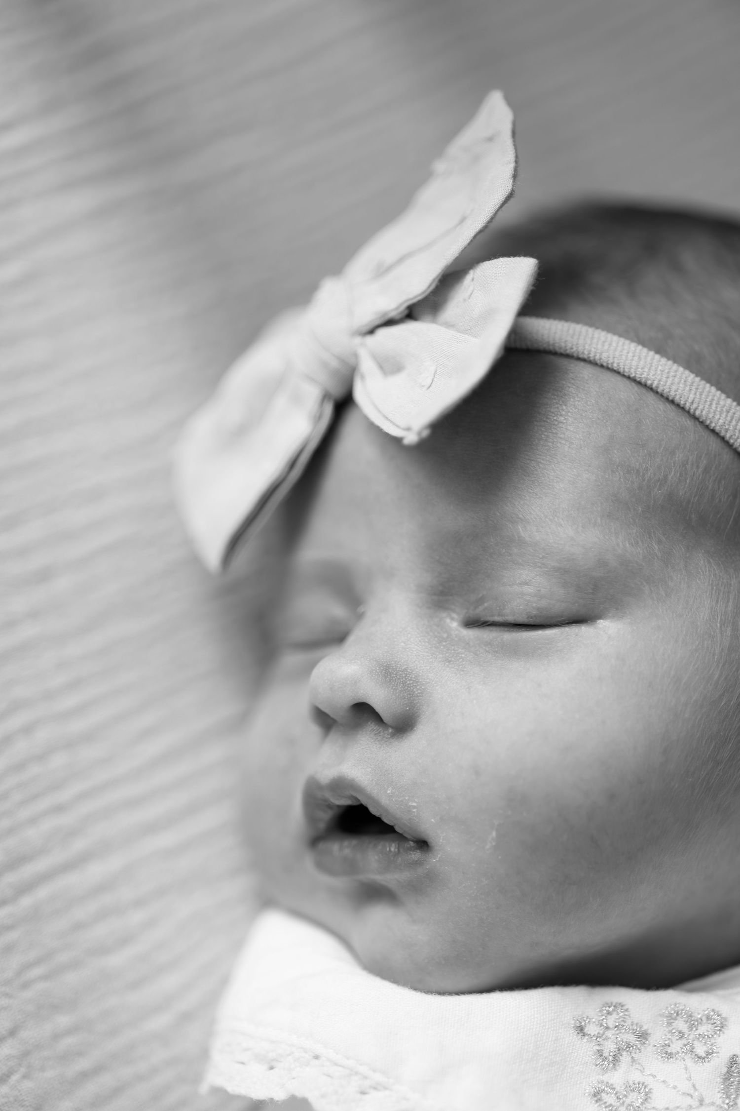 Black and white close-up of a sleeping newborn baby with a bow headband.