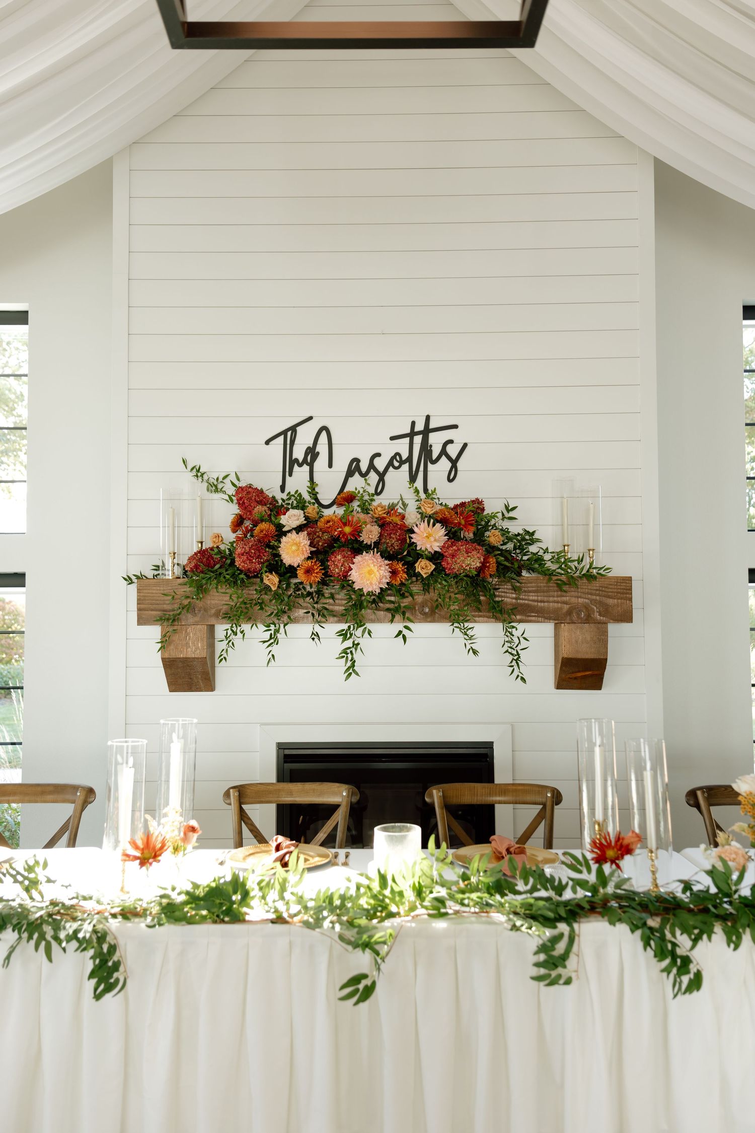 Wedding head table decorated with lush orange floral arrangements beneath a custom The Casoths metal sign.