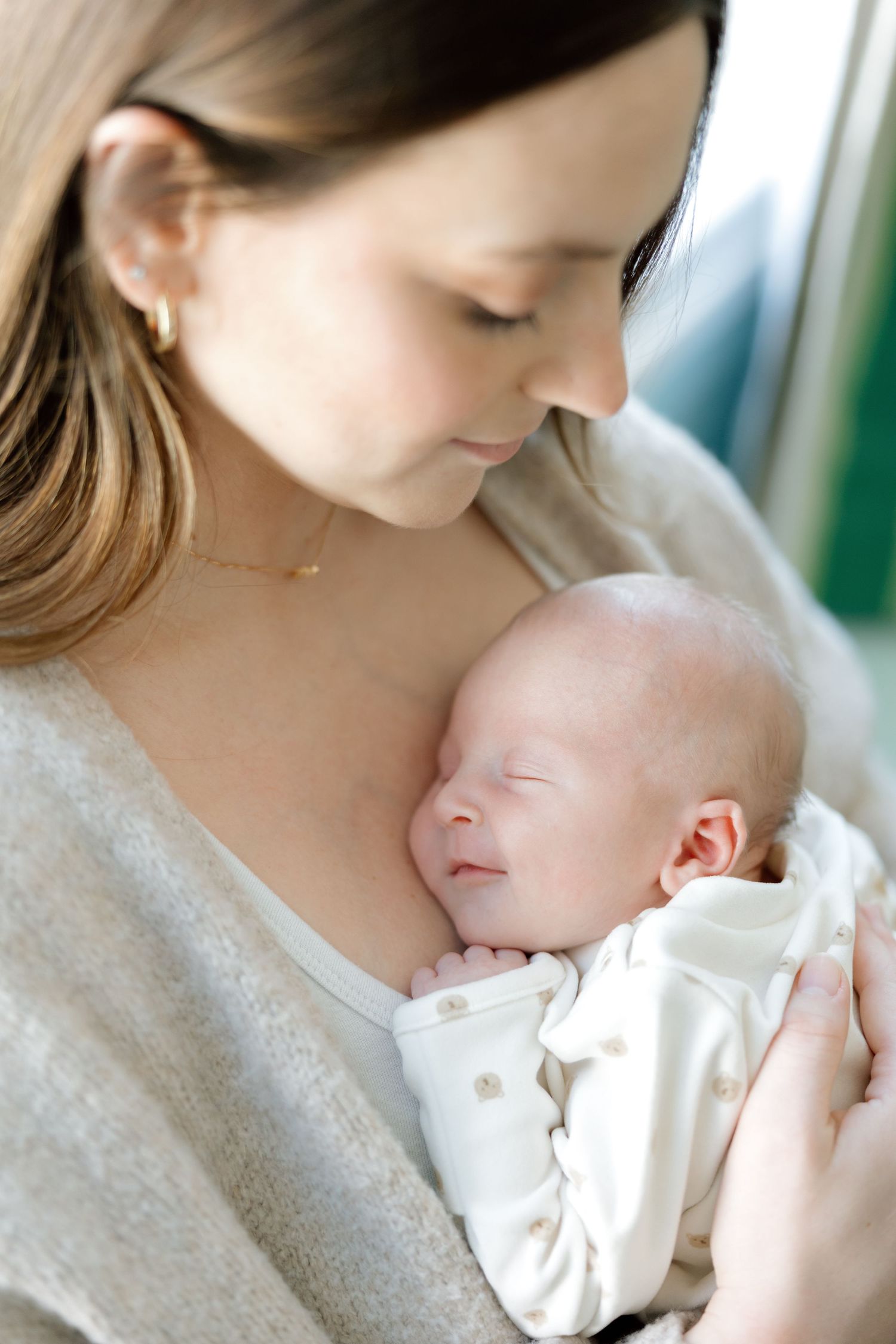 A mother tenderly holds her sleeping newborn baby dressed in white, sharing a peaceful bonding moment.