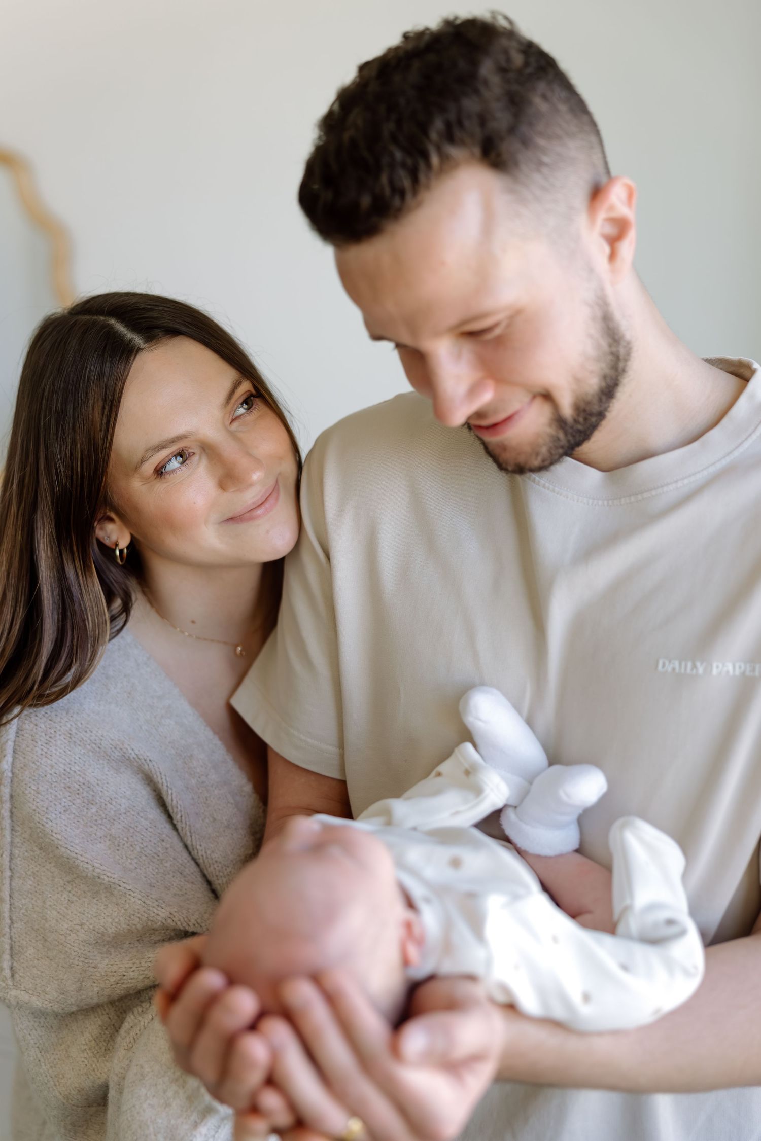 Happy young parents smiling and holding their newborn baby together in a bright room.