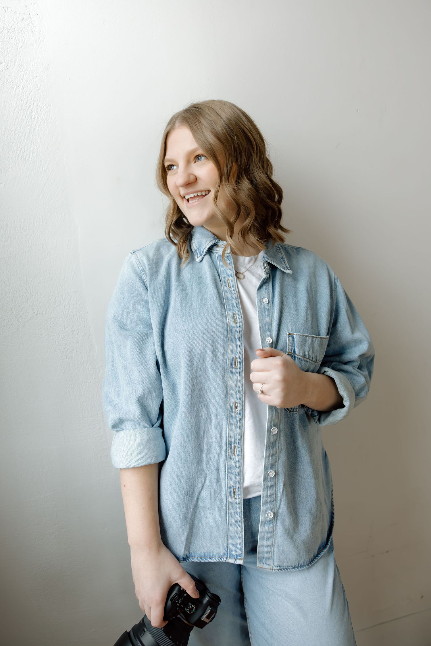 Happy female photographer in denim shirt laughing while holding a DSLR camera.