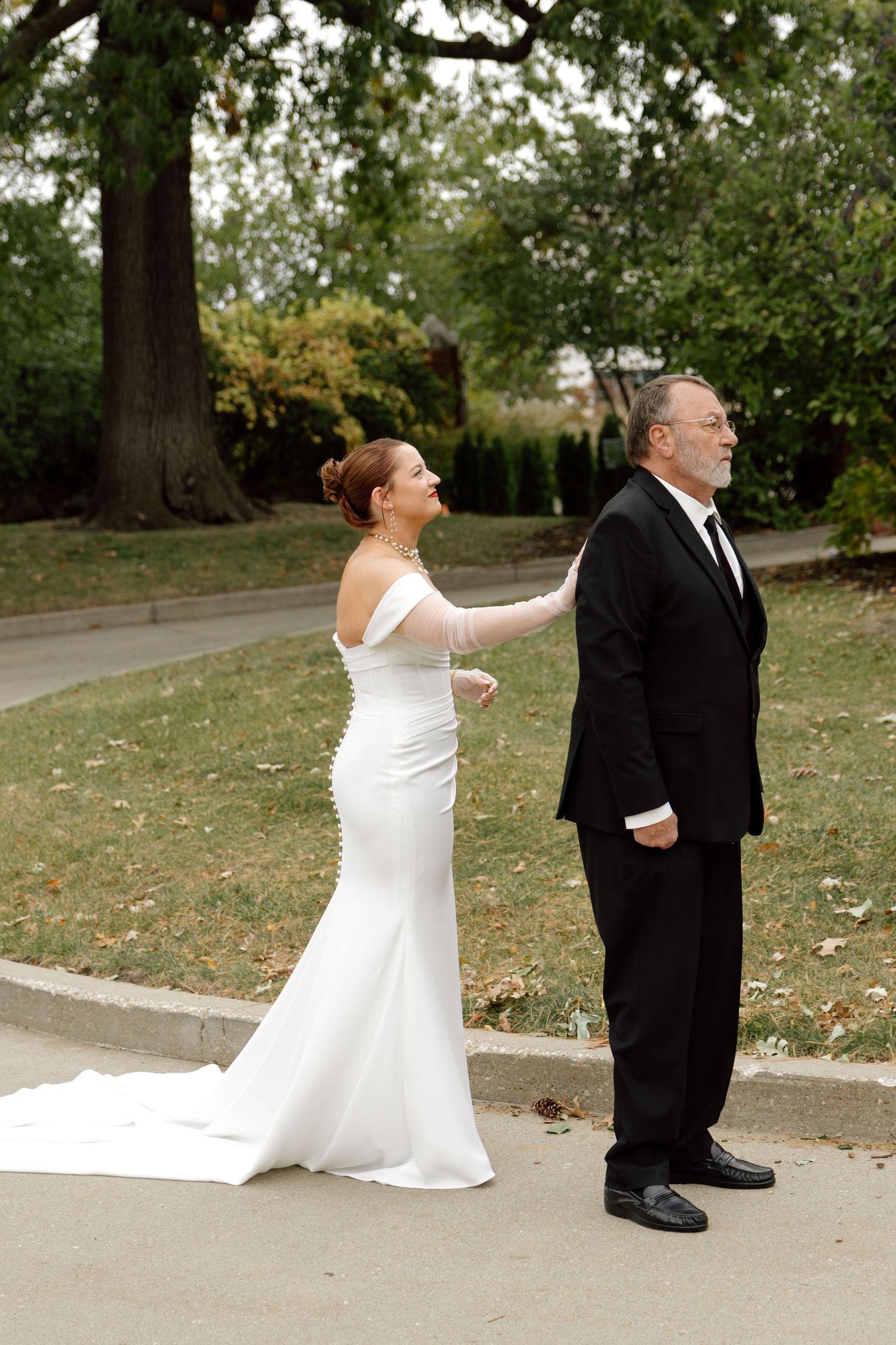 A bride in a white off-shoulder gown surprises her groom during an emotional first look outdoors.
