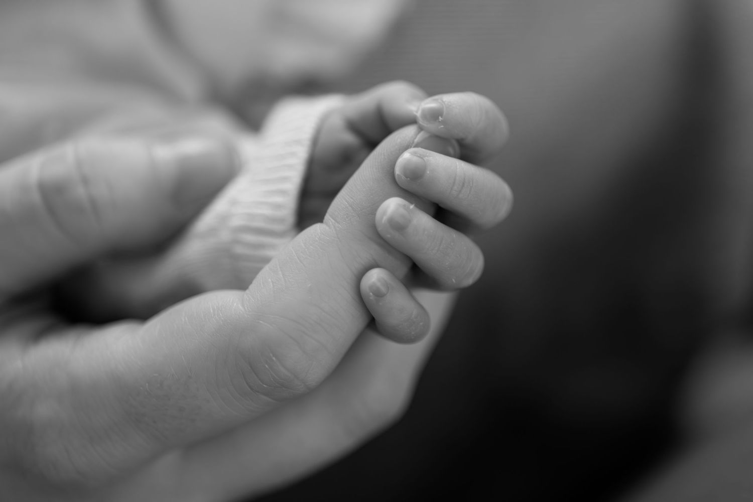 Black and white macro photo of newborn baby holding parent's finger.