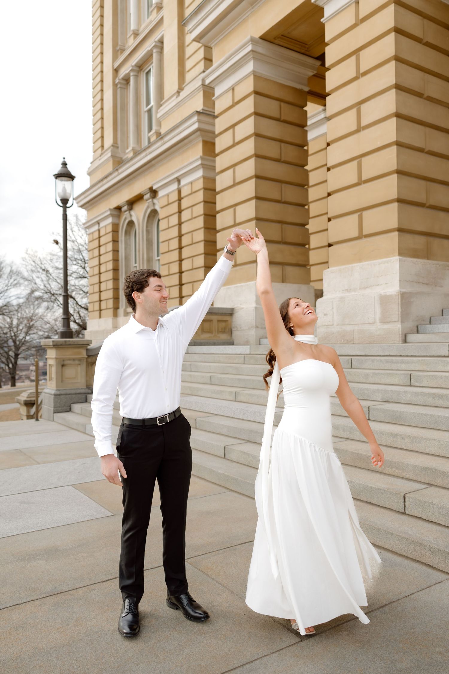 Joyful couple in wedding attire dancing and twirling on steps of grand stone building on their wedding day.