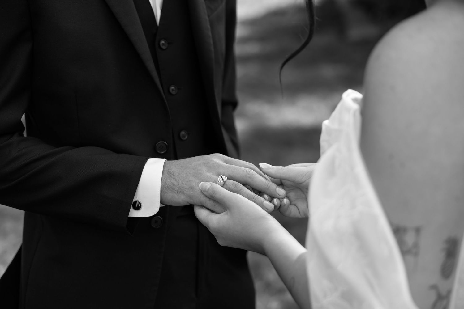 Black and white close-up of groom placing a wedding ring on the brides hand during the ceremony.
