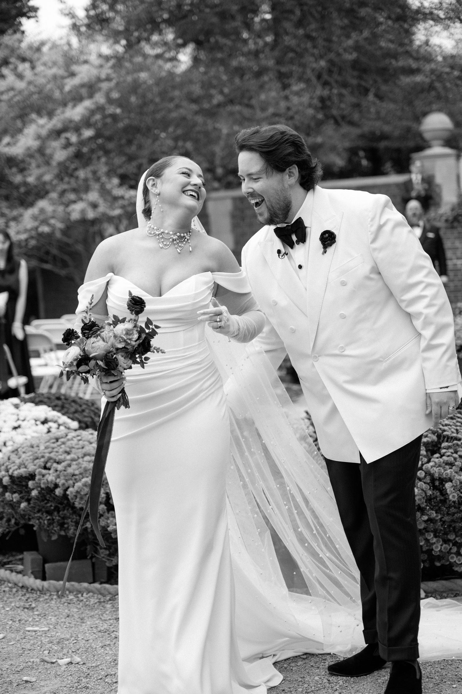 Black and white photo of laughing bride and groom walking together after outdoor ceremony.