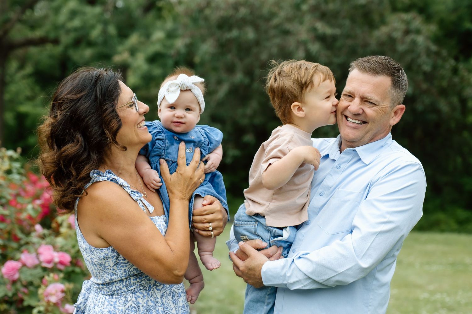 Happy family portrait with parents holding two young children in a rose garden.
