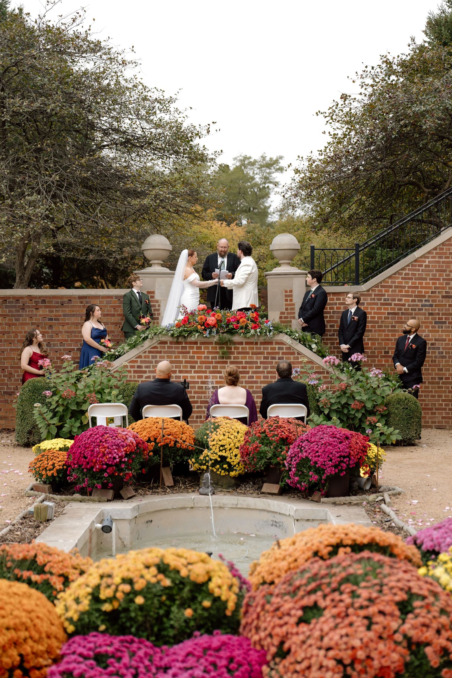 Small intimate outdoor fall wedding ceremony surrounded by vibrant chrysanthemums and brick staircase.