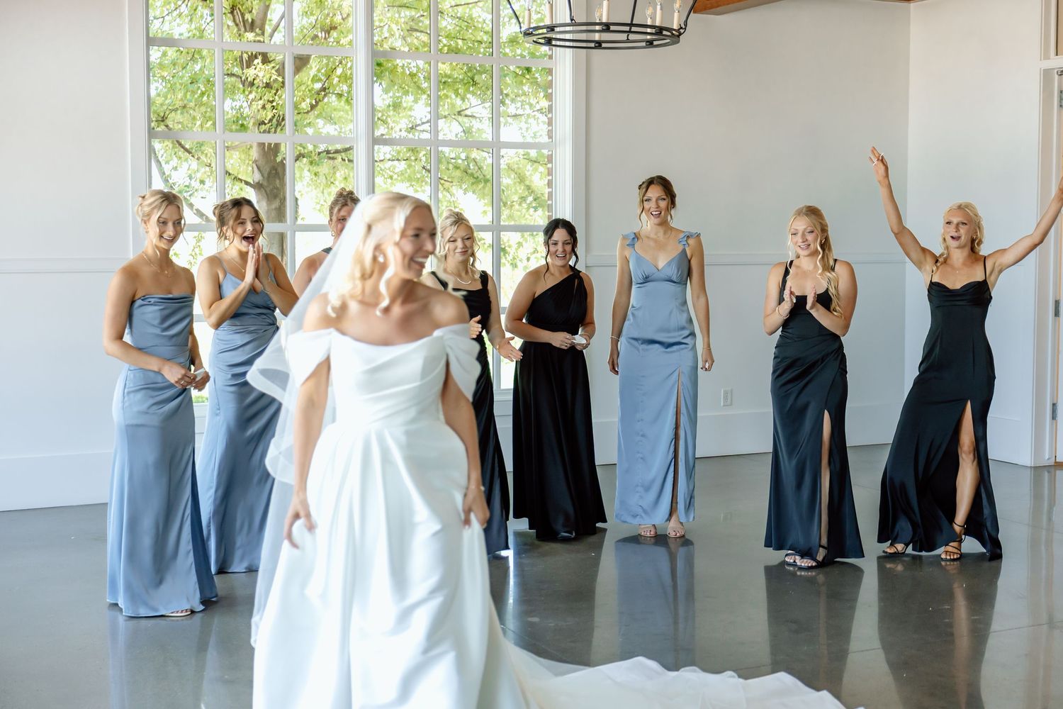 Bride first look as excited bridesmaids in blue and black dresses react behind her at The Monroe wedding venue in West Des Moines, Iowa.