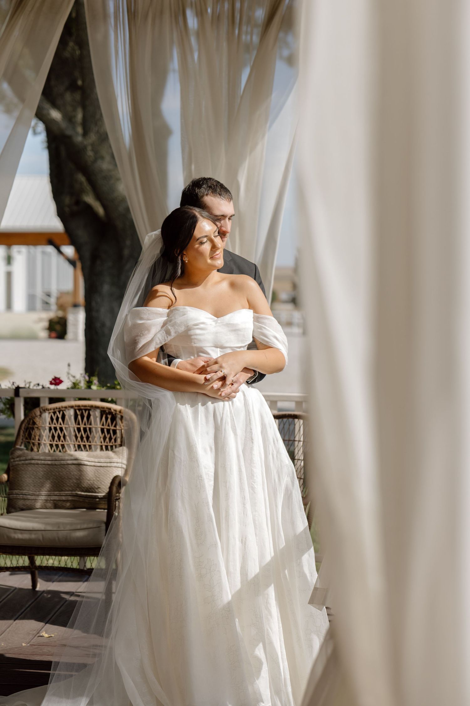 Bride and groom embracing under white flowing curtains at elegant outdoor wedding venue.