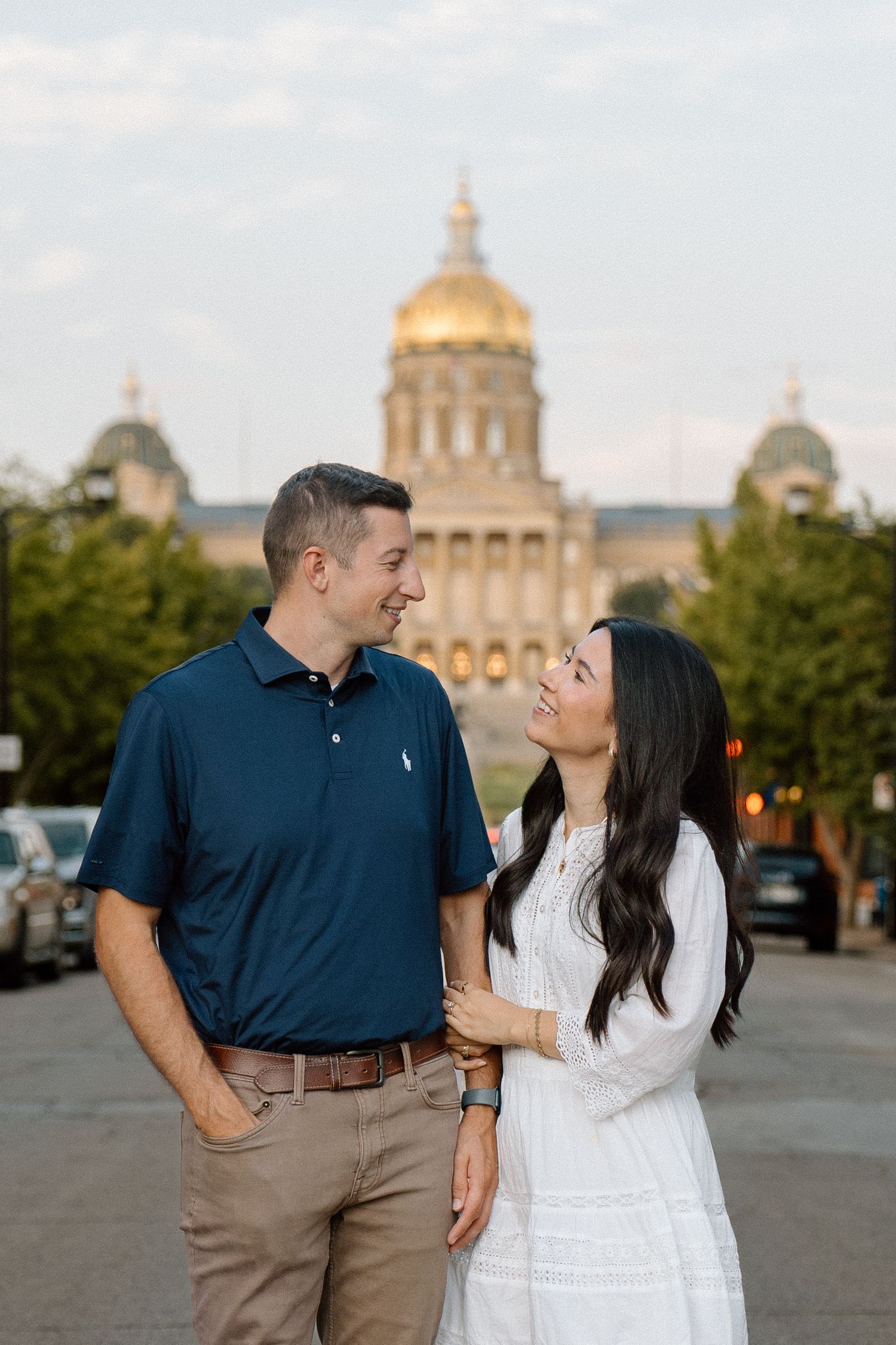 Happy couple gazing at each other with the golden-domed Iowa State Capitol building glowing behind them at dusk.