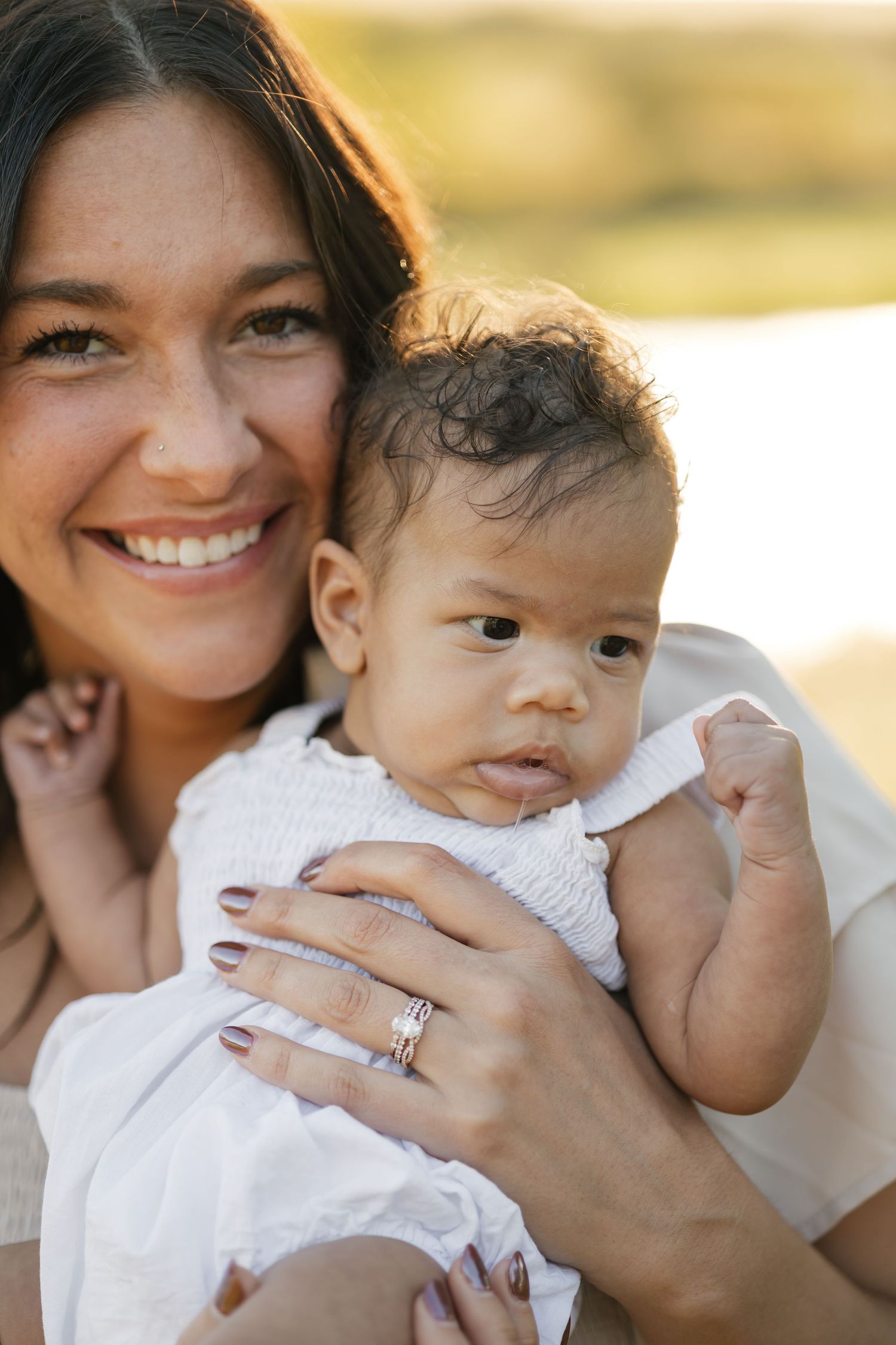 Smiling mother with freckles holding infant baby outdoors in warm sunlight.
