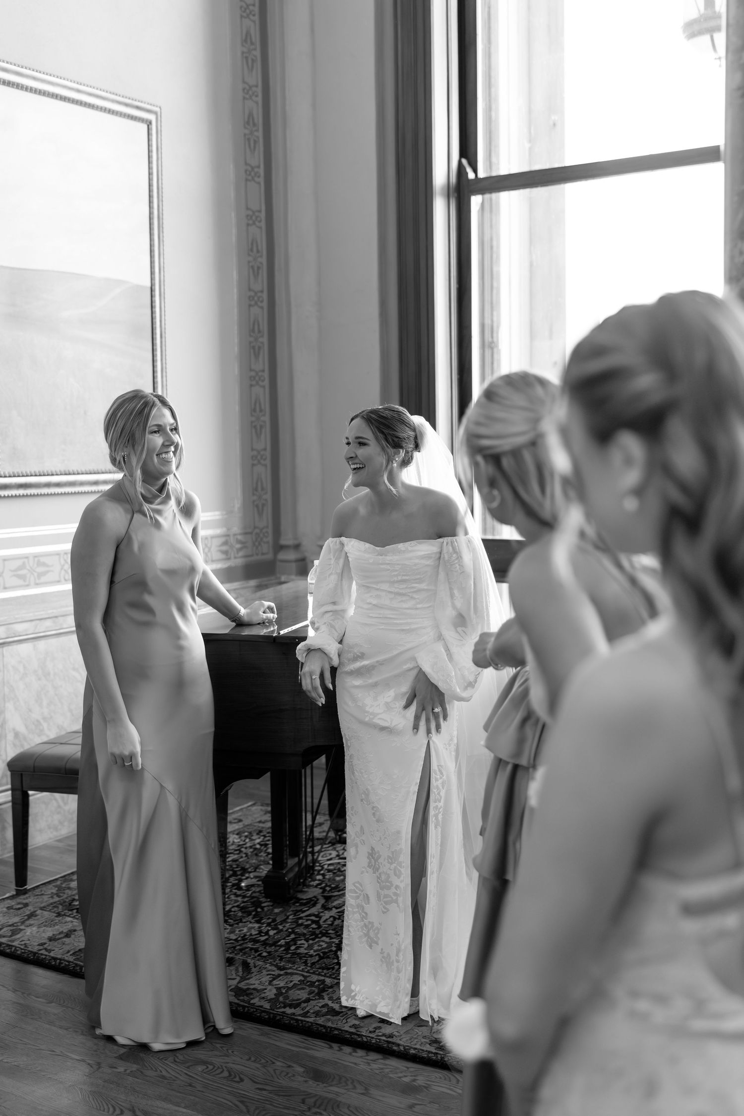 Bride laughing with bridesmaids in elegant room before wedding ceremony in black and white photo.