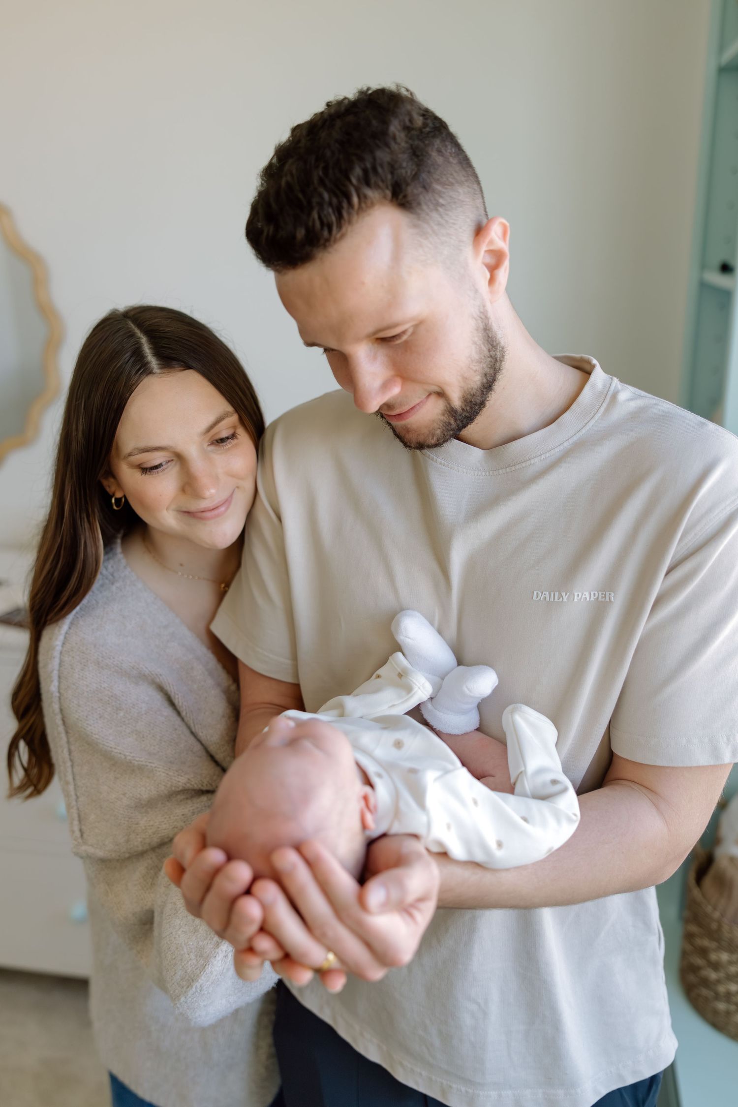 New parents cradle their newborn baby in their hands, gazing down lovingly in a softly lit room.