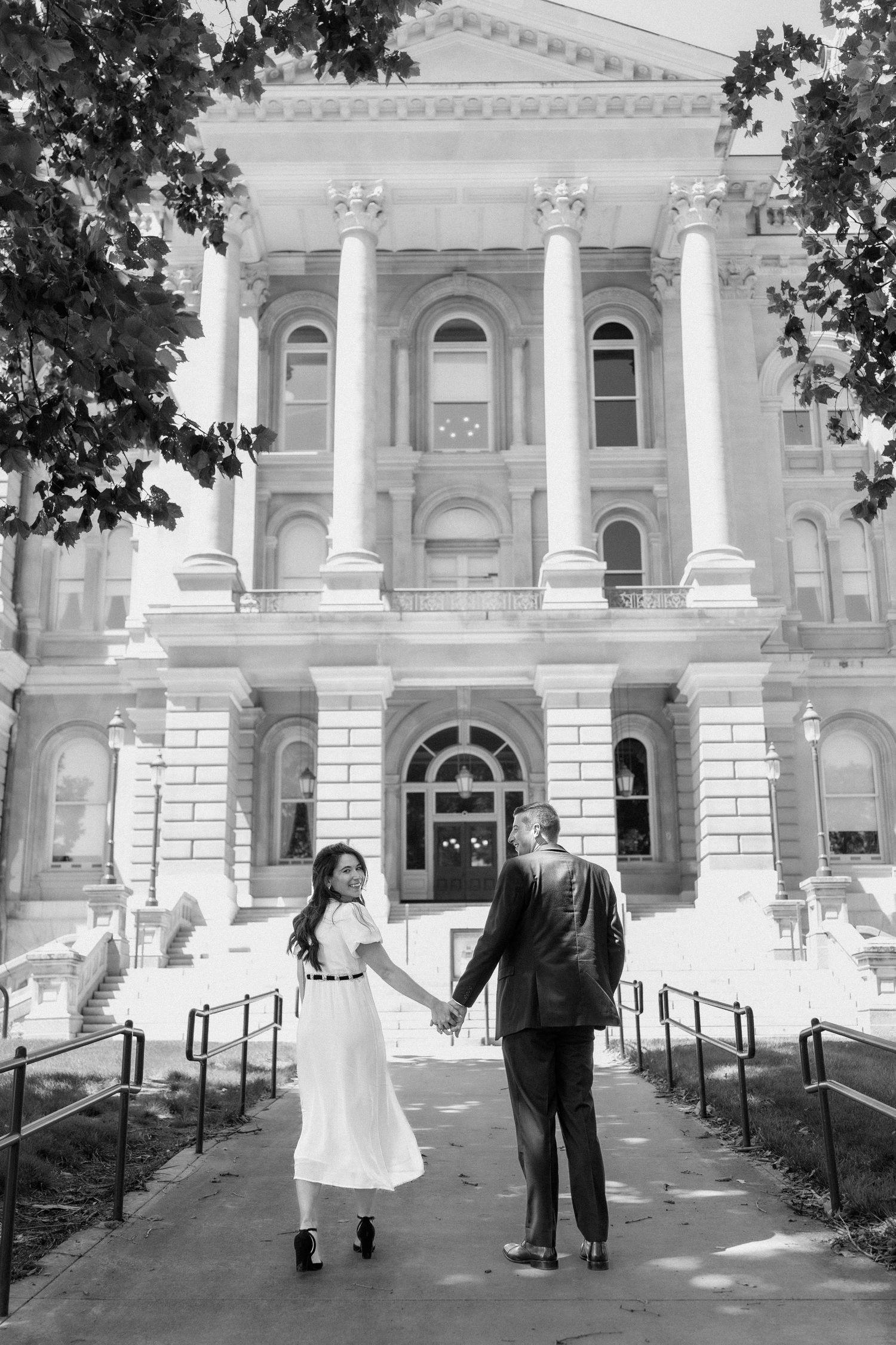 Black and white photo of couple holding hands before a grand neoclassical building with columns.