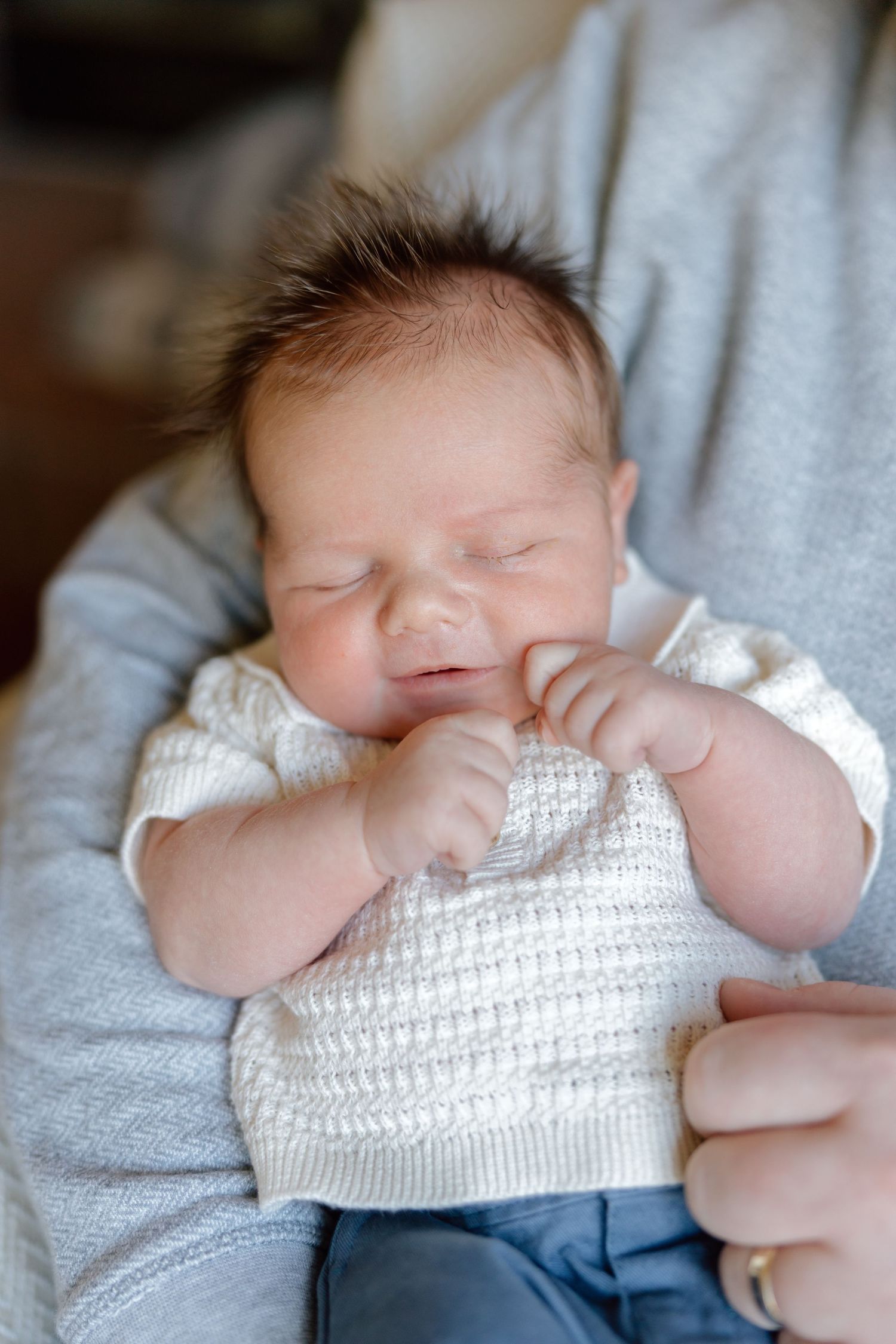 Close-up of a sleeping newborn baby with dark hair resting in arms.