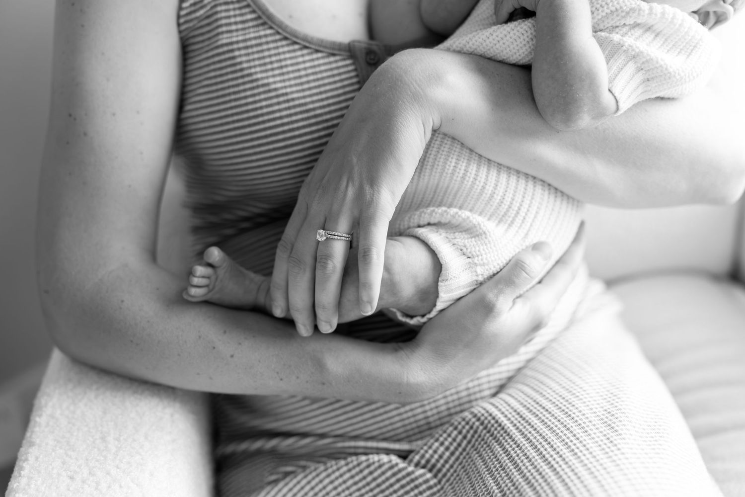 Black and white photo of a mother cradling her newborn baby, showing tender hands and tiny feet.