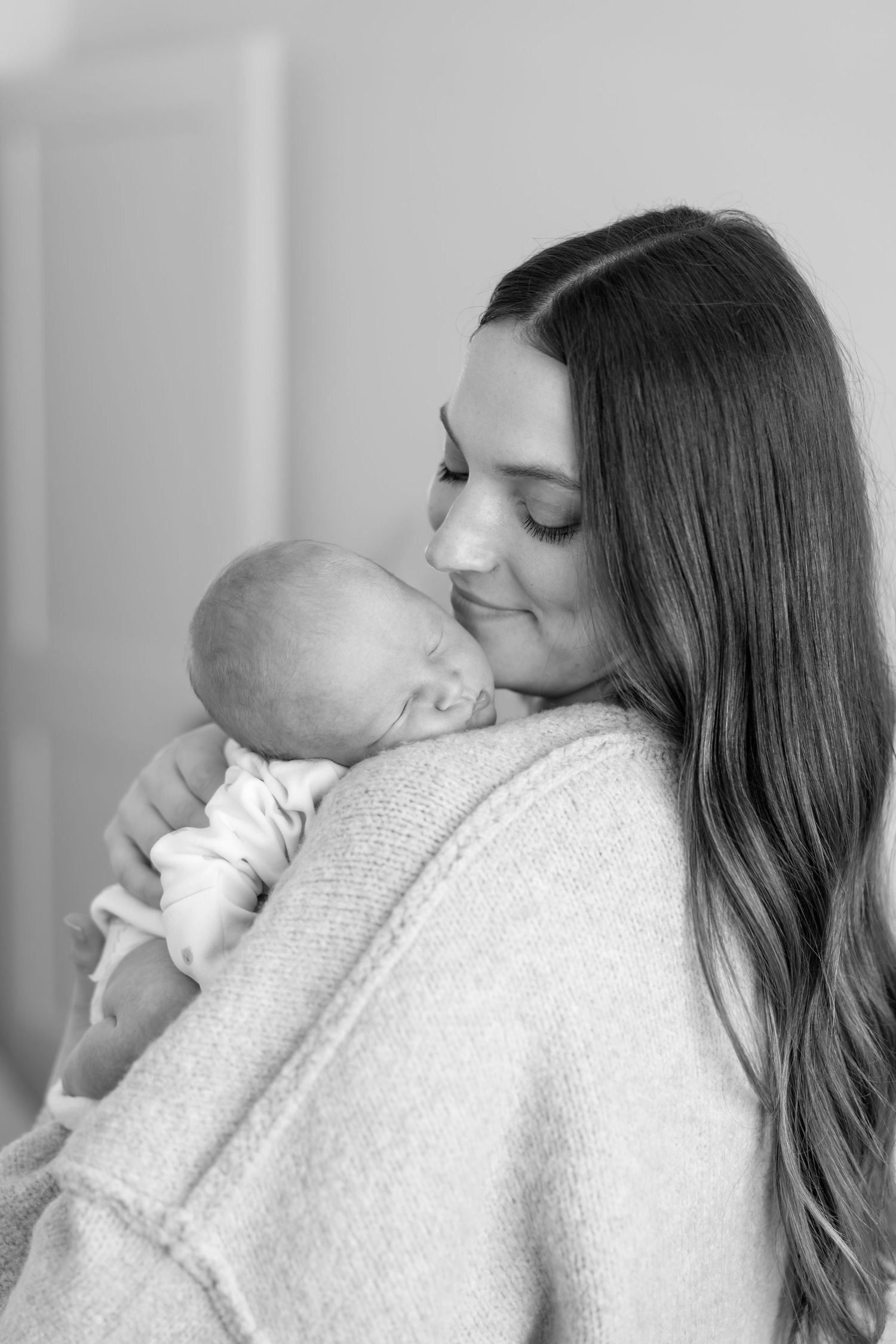 Black and white portrait of a mother smiling and cuddling her sleeping newborn baby.