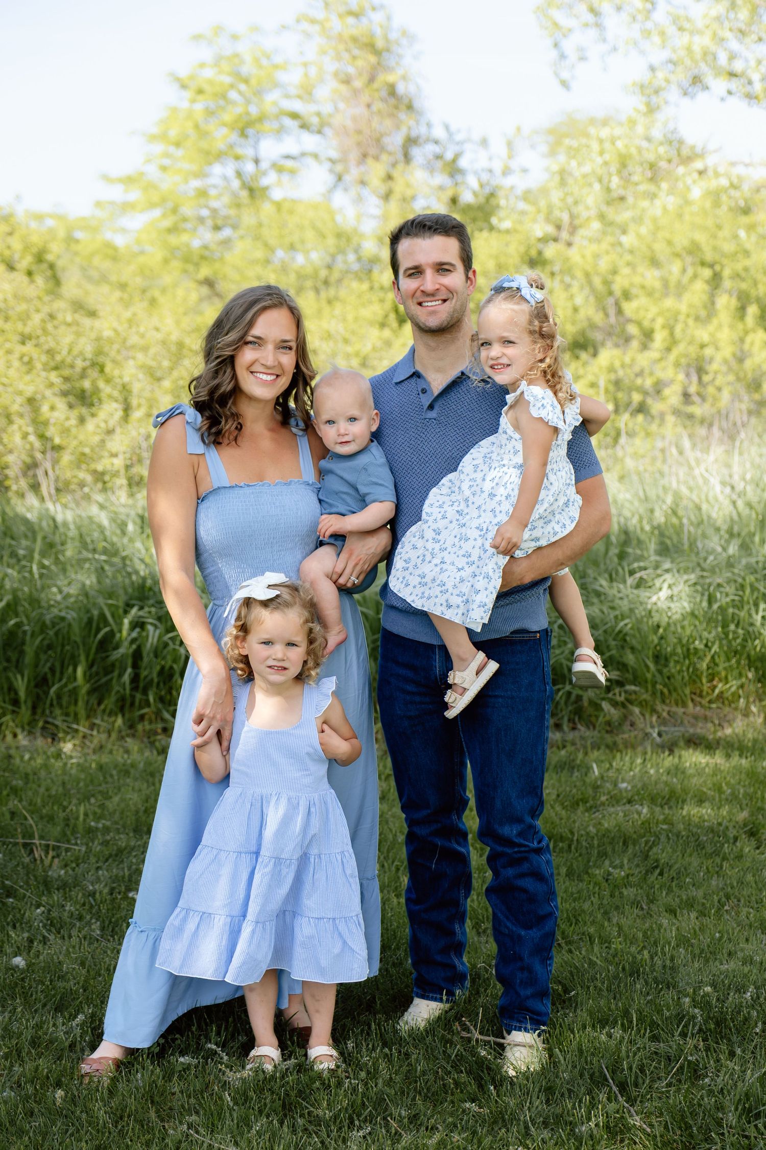 Family of five posing outdoors in coordinating blue outfits in a green meadow.
