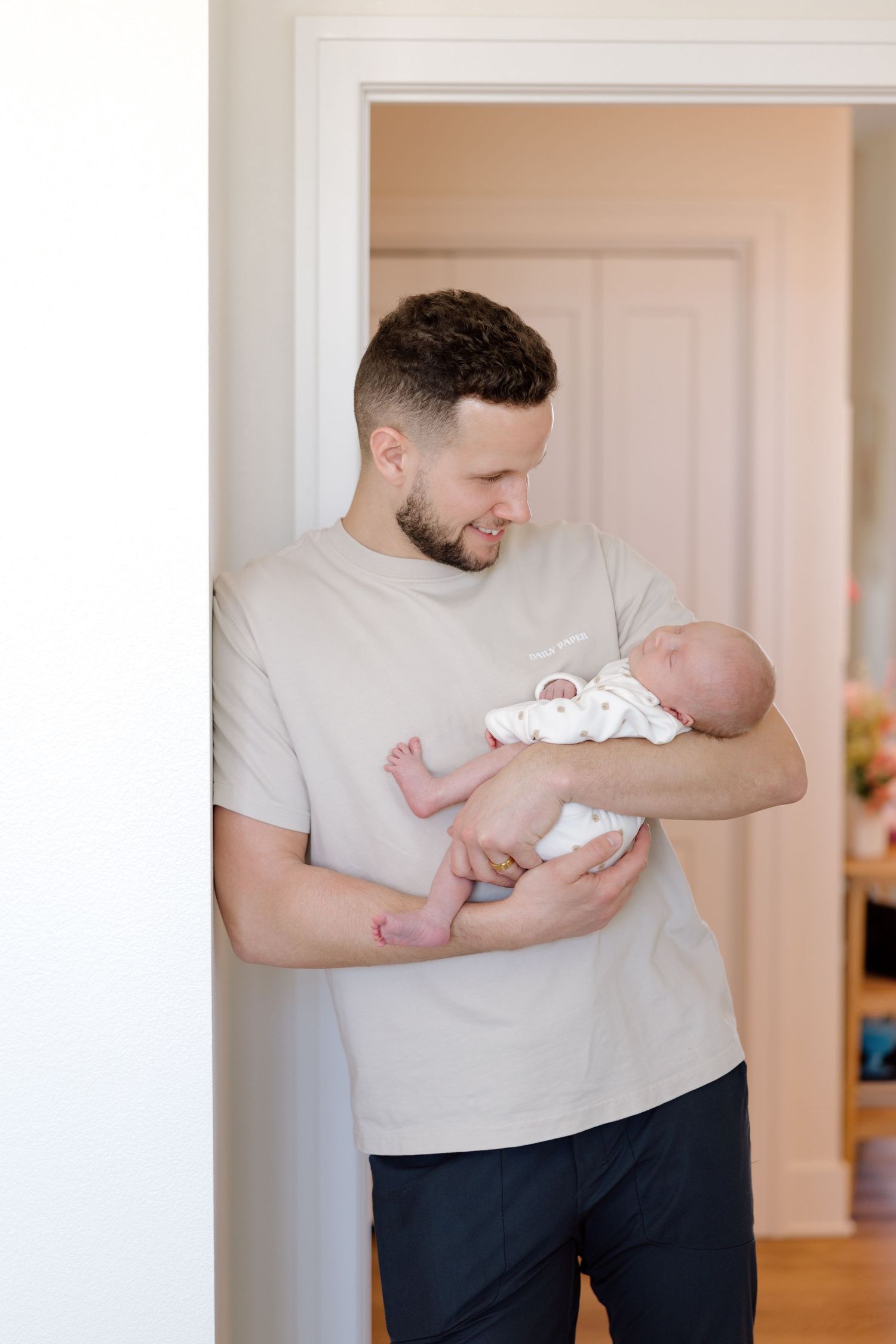 A smiling father stands in a doorway carefully cradling his newborn baby in his arms.