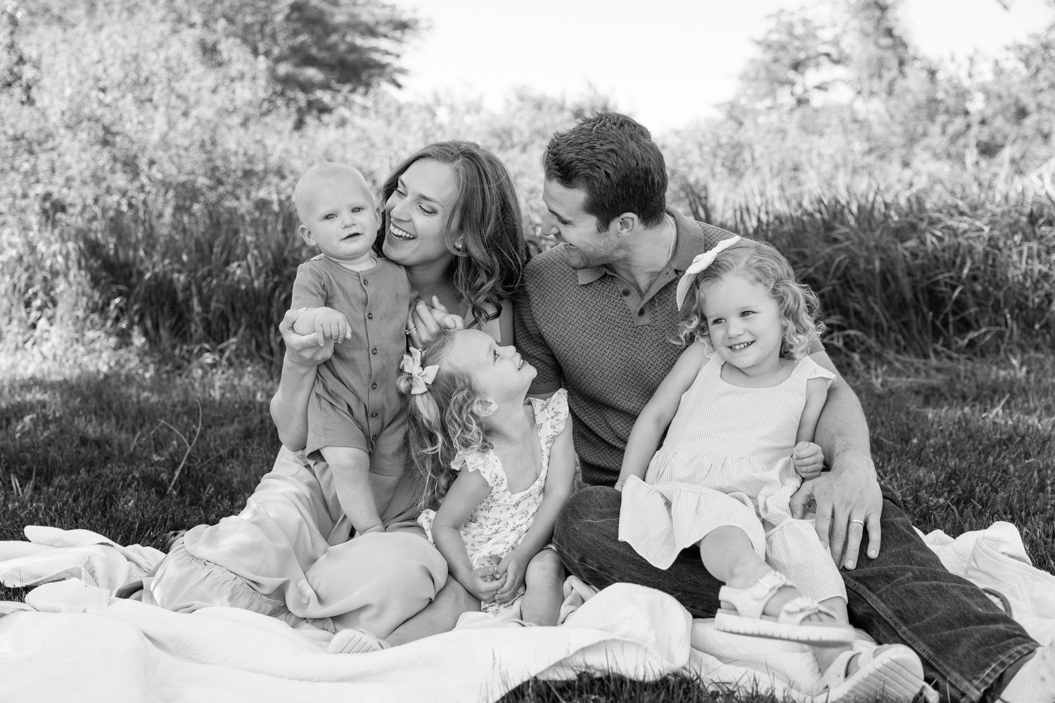 Black and white photo of a happy family of five cuddling on a blanket outdoors.