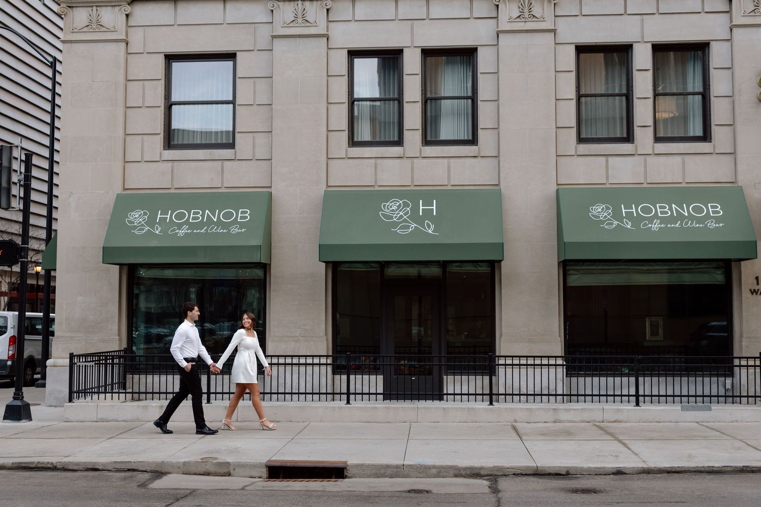 Couple walking past Hobnob restaurant with green awnings on a city street.