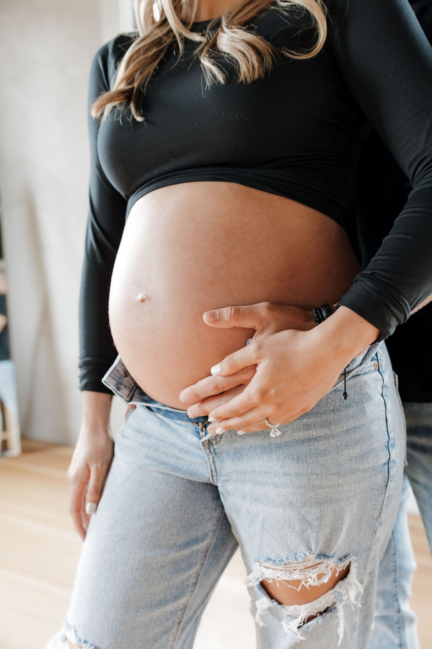 Close-up of a pregnant woman in a black top and ripped jeans cradling her bare baby bump.