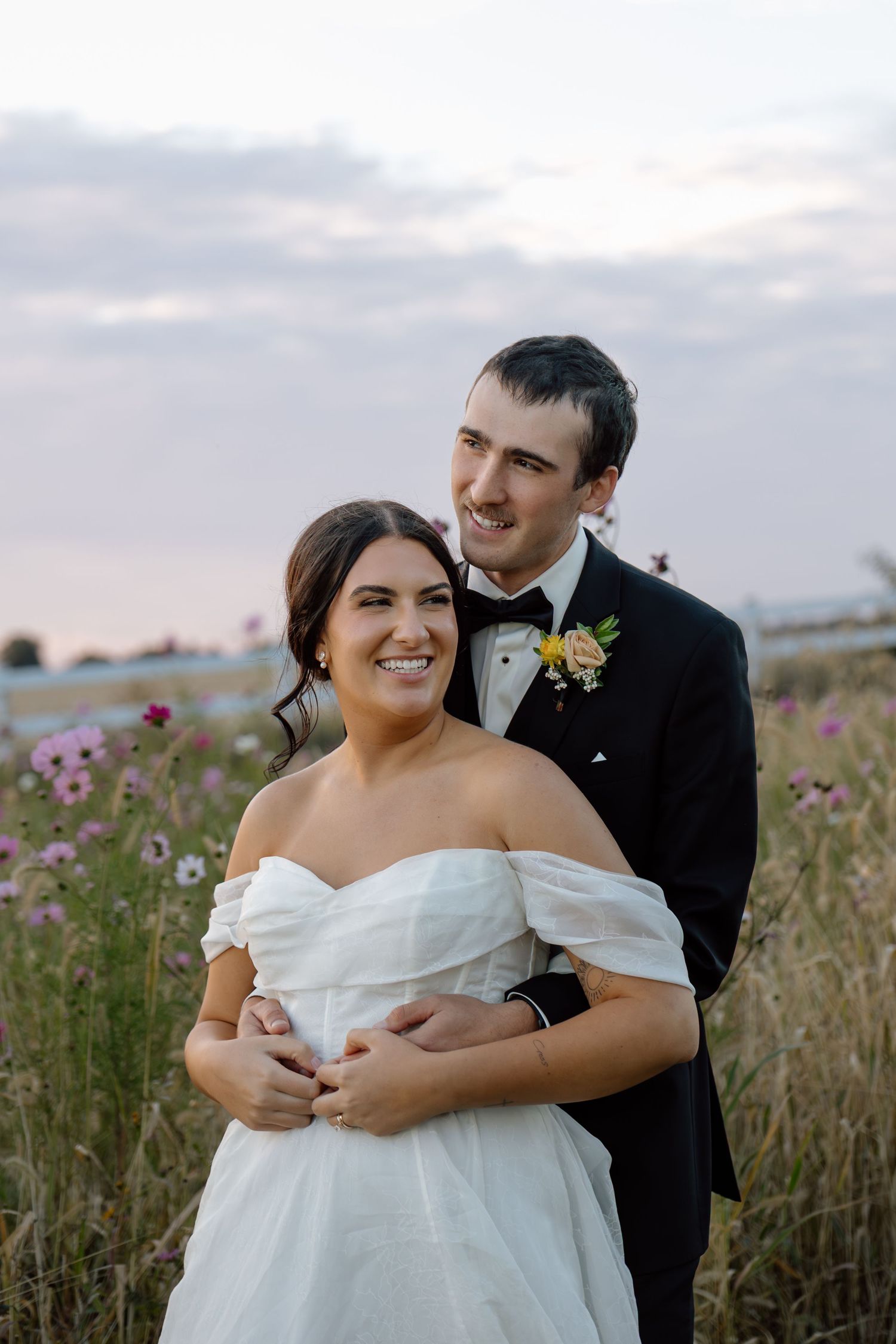 Smiling bride and groom embrace in a wildflower field at sunset during their wedding day.