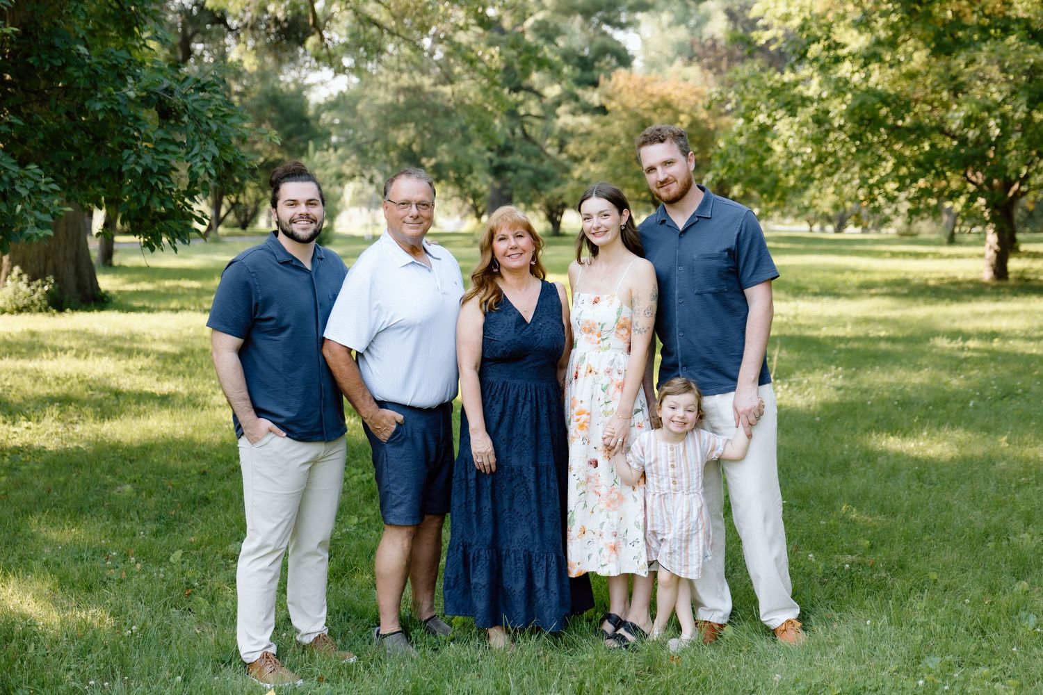 Extended family of six adults and one child posing together in a lush green park setting.