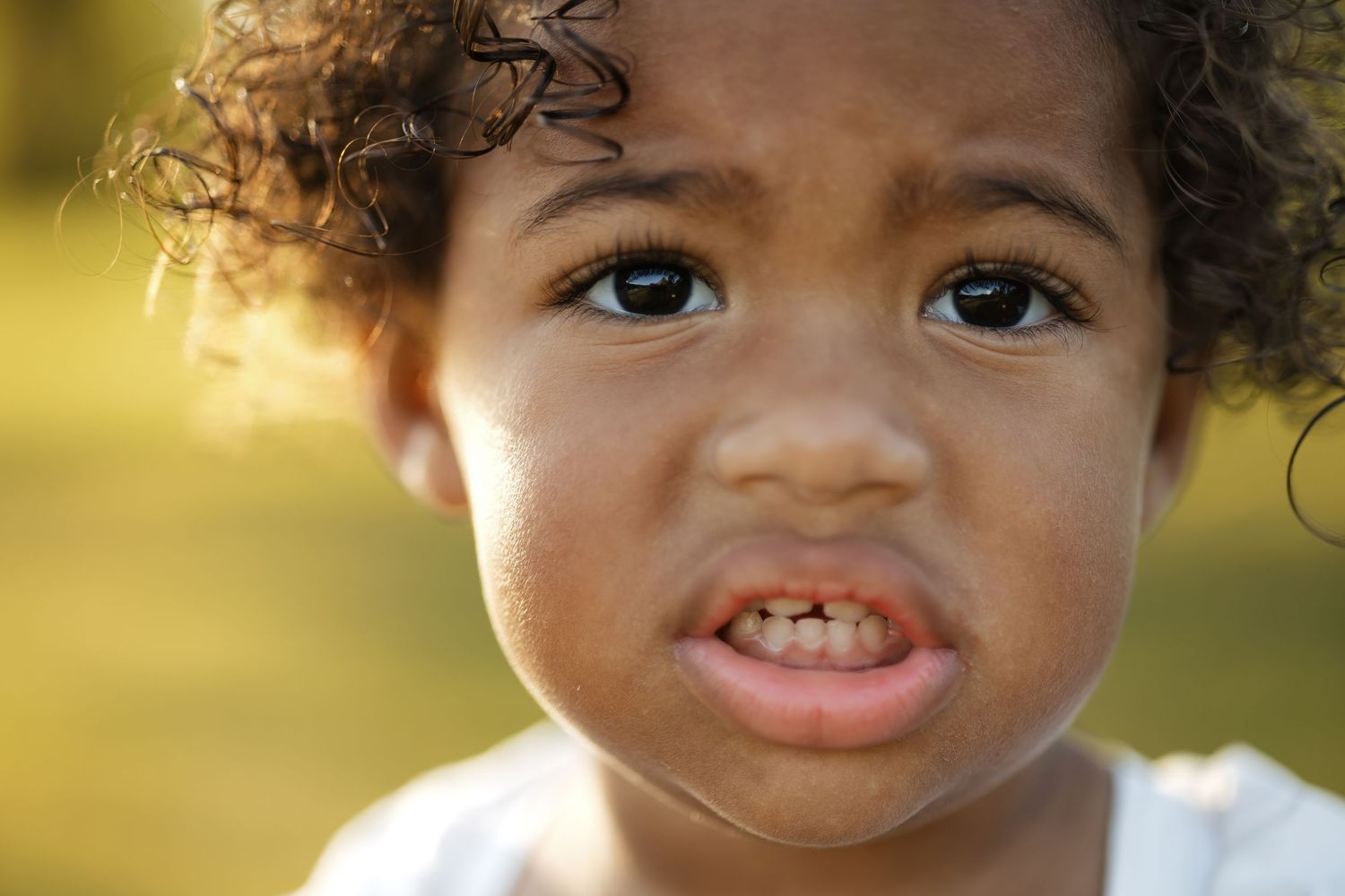 Close-up portrait of a young toddler with curly hair and brown eyes outdoors.