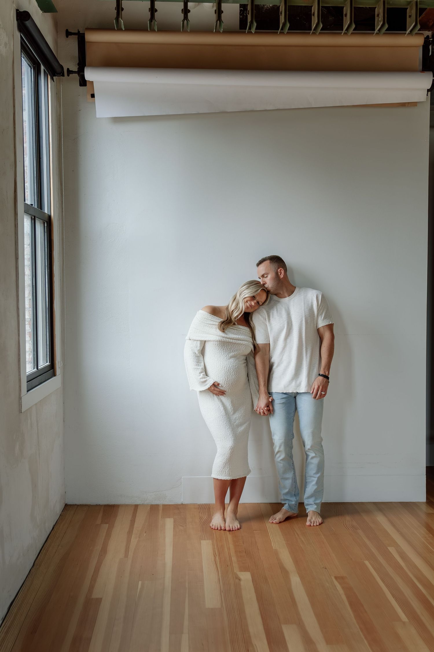 Couple sharing tender moment during maternity photoshoot, man kissing pregnant womans head.