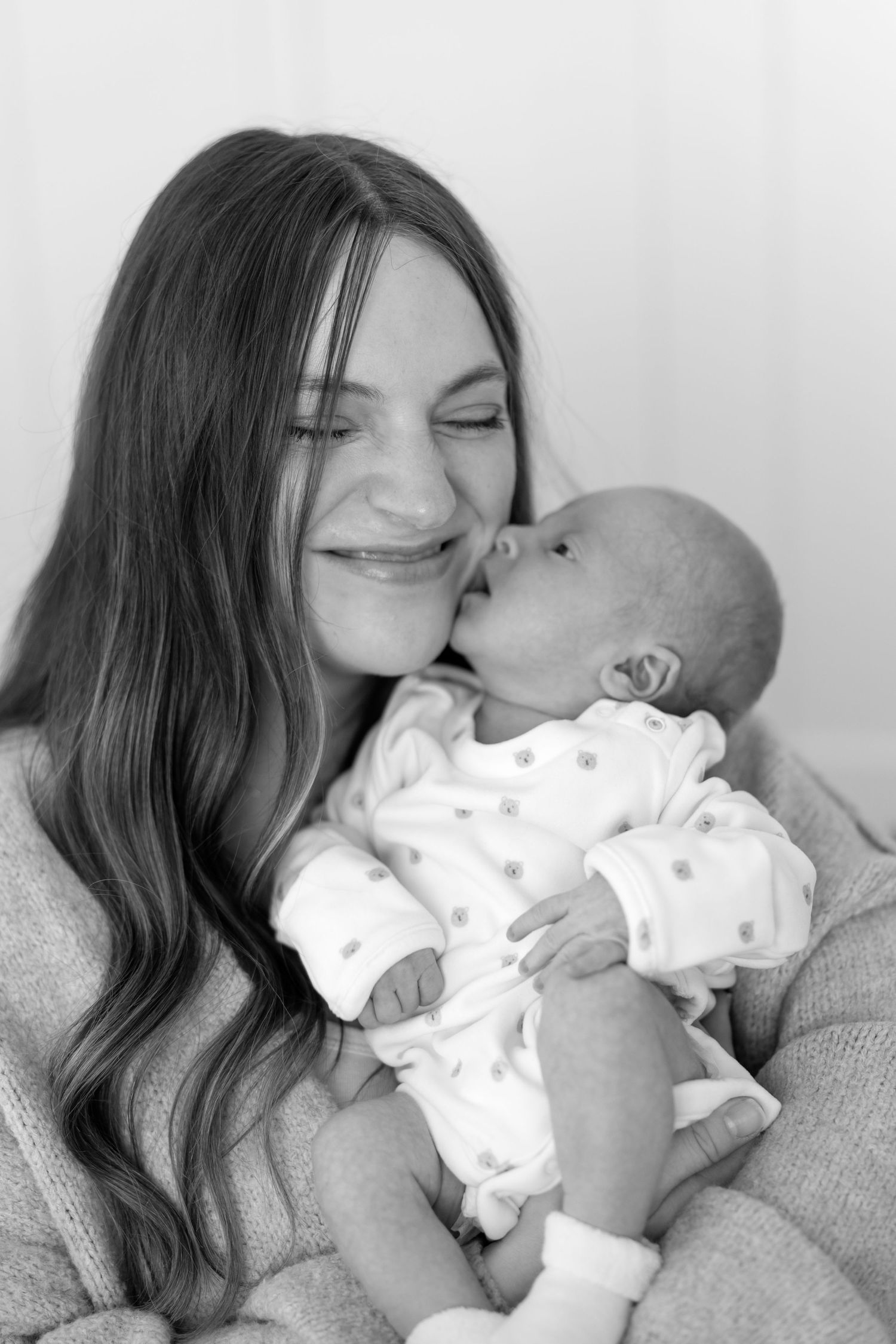 Black and white photo of a smiling mother holding and kissing her newborn baby.