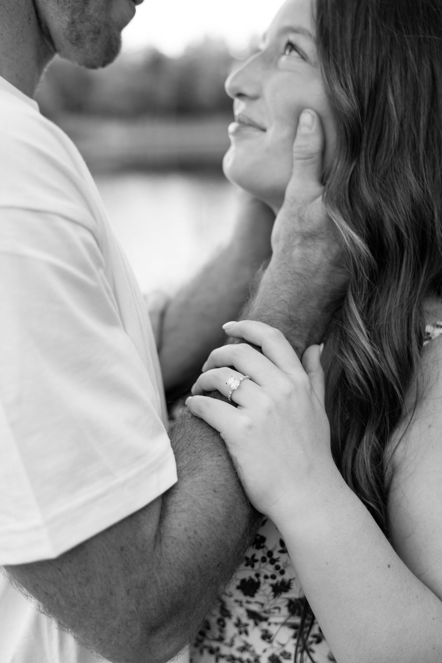 Black and white close-up of couple almost kissing, woman showing off diamond engagement ring.
