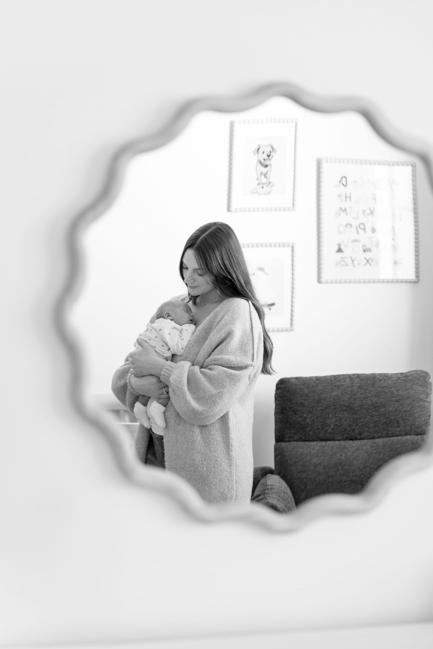 Black and white mirror reflection of a mother tenderly holding her newborn in a nursery.