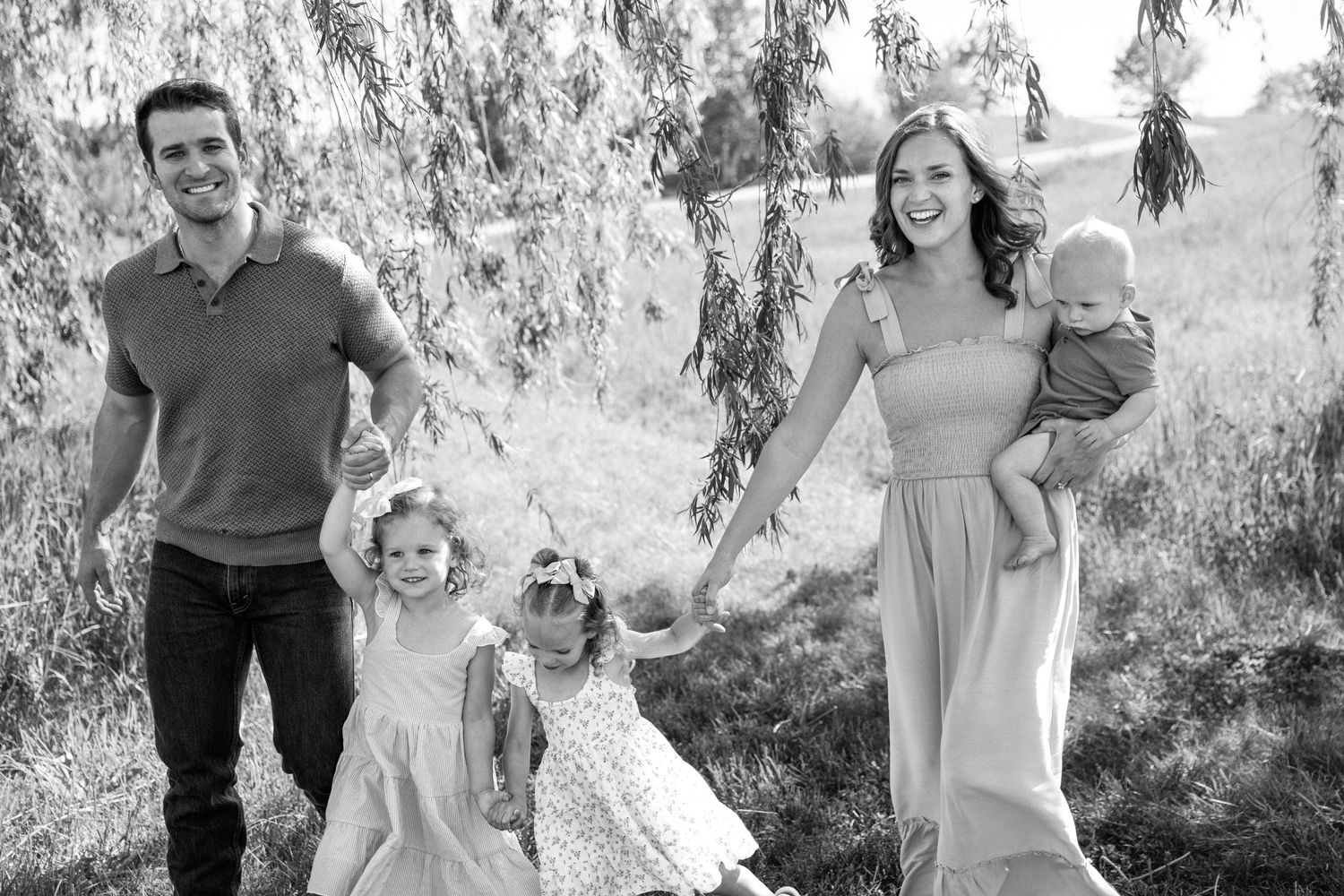 Black and white photo of a family of five walking outdoors under a willow tree.