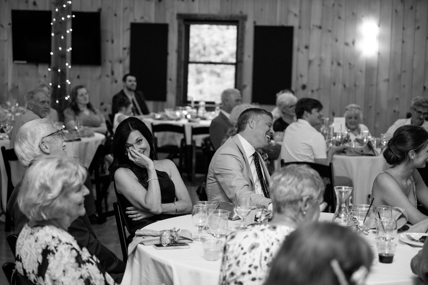 Black and white candid photo of wedding guests laughing and enjoying themselves during the reception dinner.