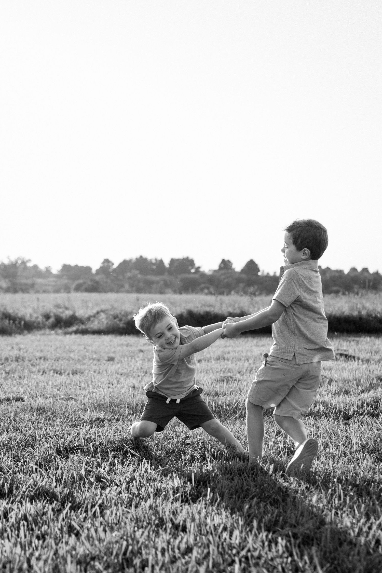 Black and white photo of two young brothers holding hands and spinning together in a grassy field.