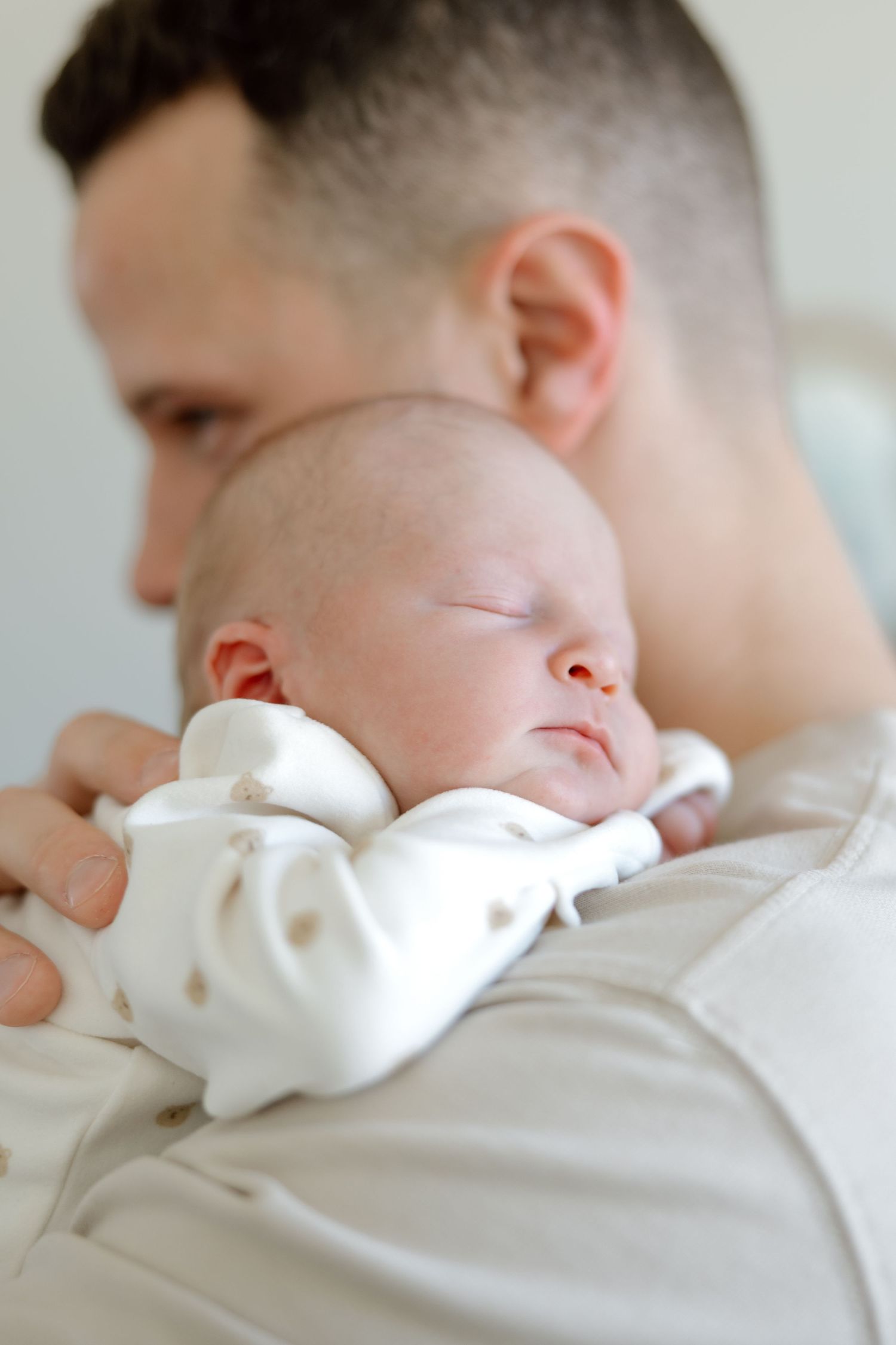 Close-up of a father holding his peacefully sleeping newborn baby against his chest.