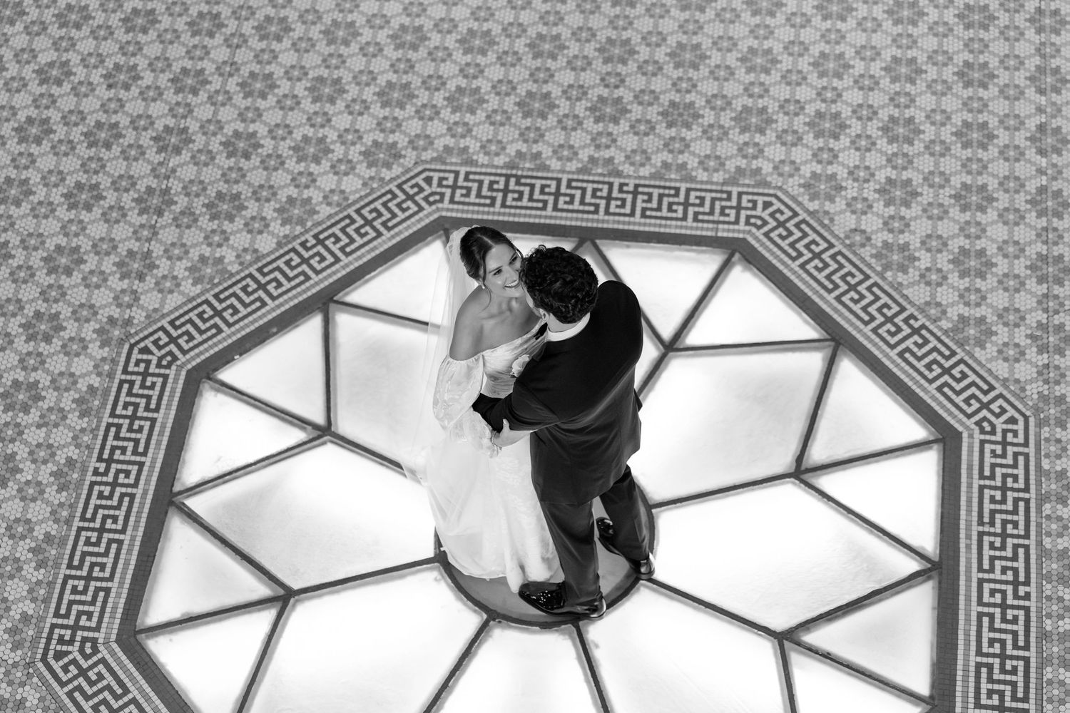 Aerial view of bride and groom sharing first dance on ornate octagonal ballroom floor.