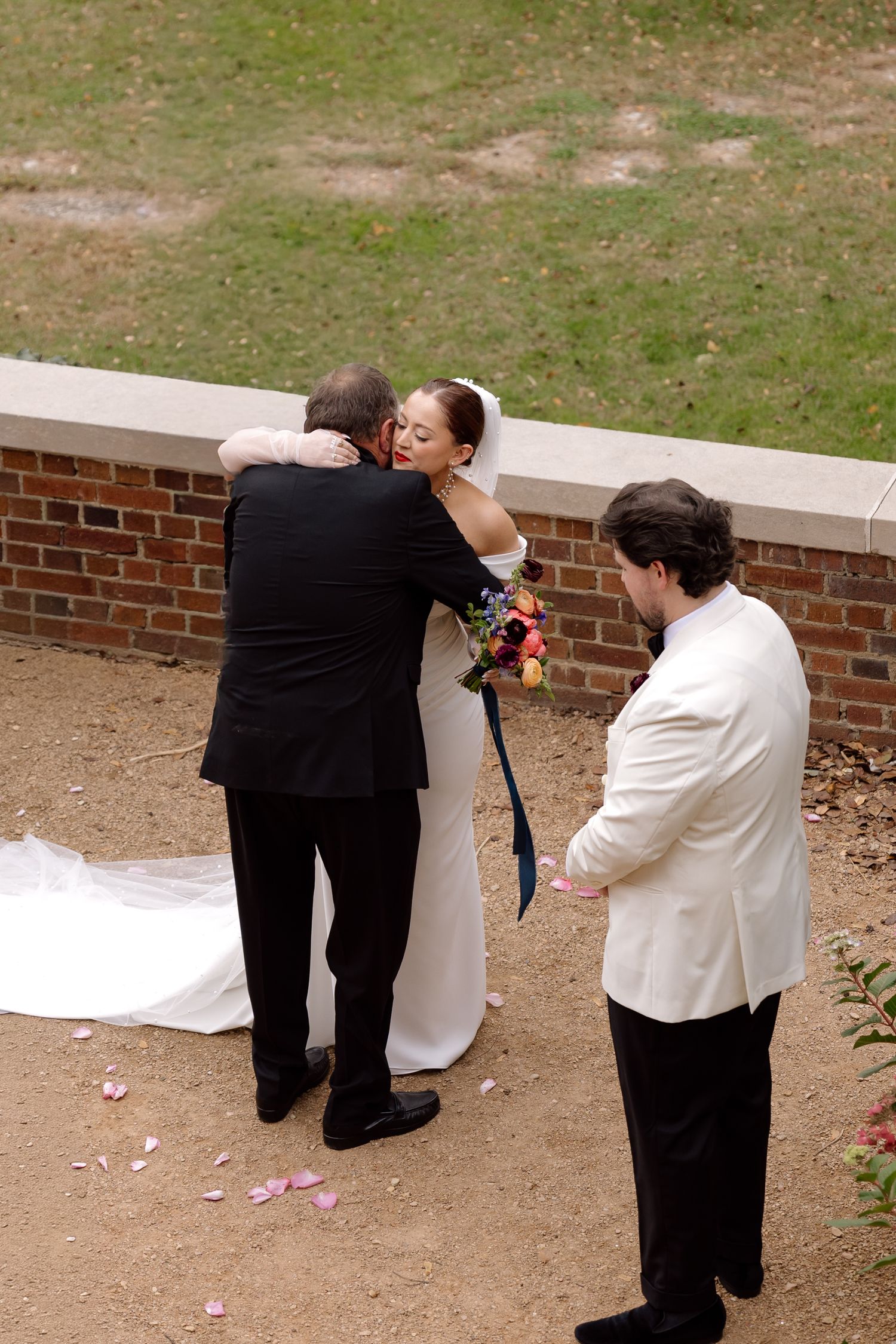 Bride and groom share a heartfelt embrace during outdoor wedding ceremony with officiant nearby.