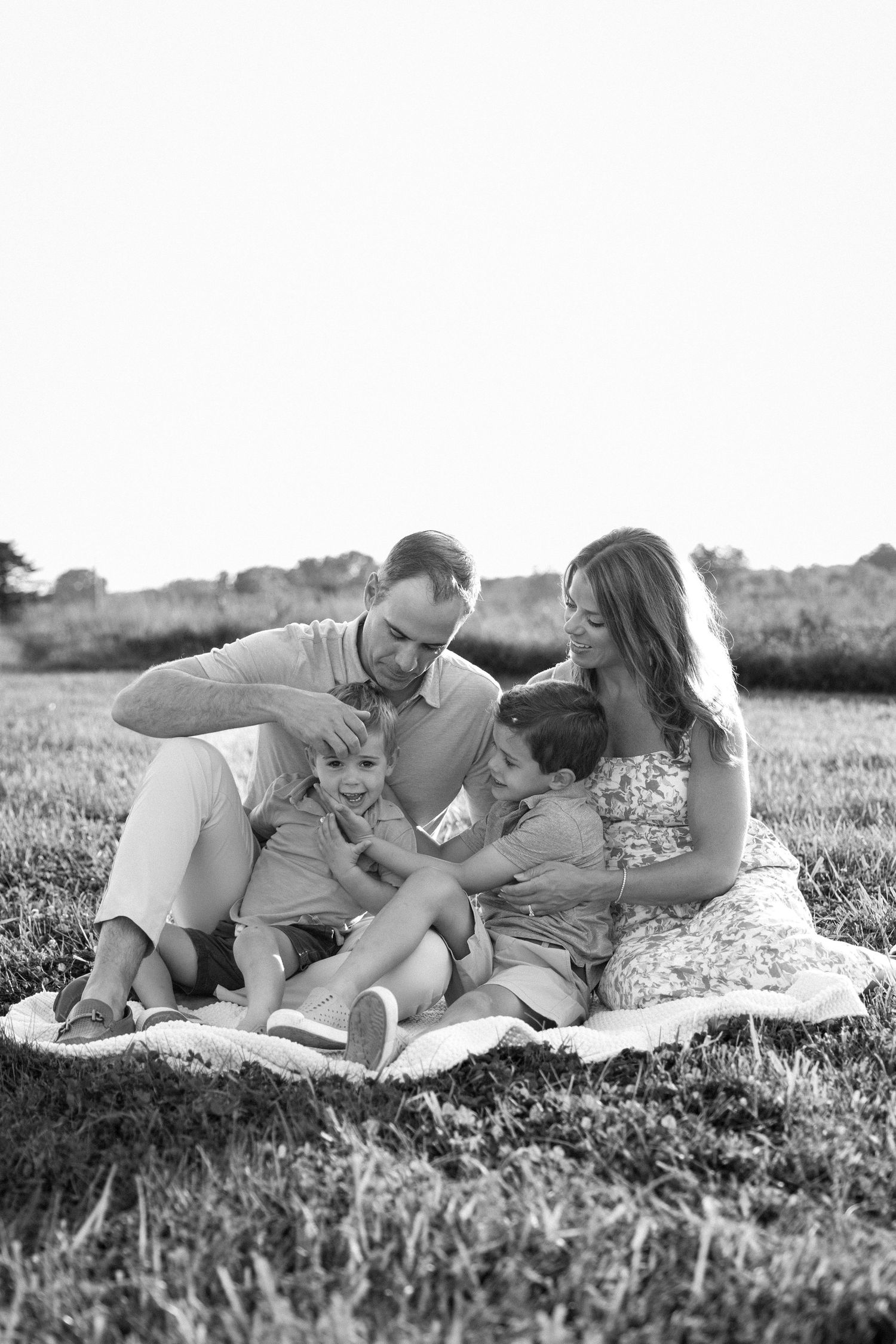 Black and white photo of a happy family of four sitting on a blanket in a grassy field.