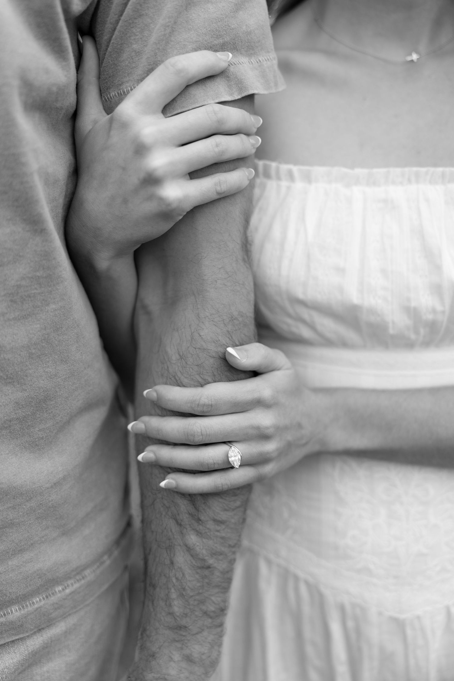 Black and white photo of a couple embracing, woman wearing an engagement ring holding mans arm.